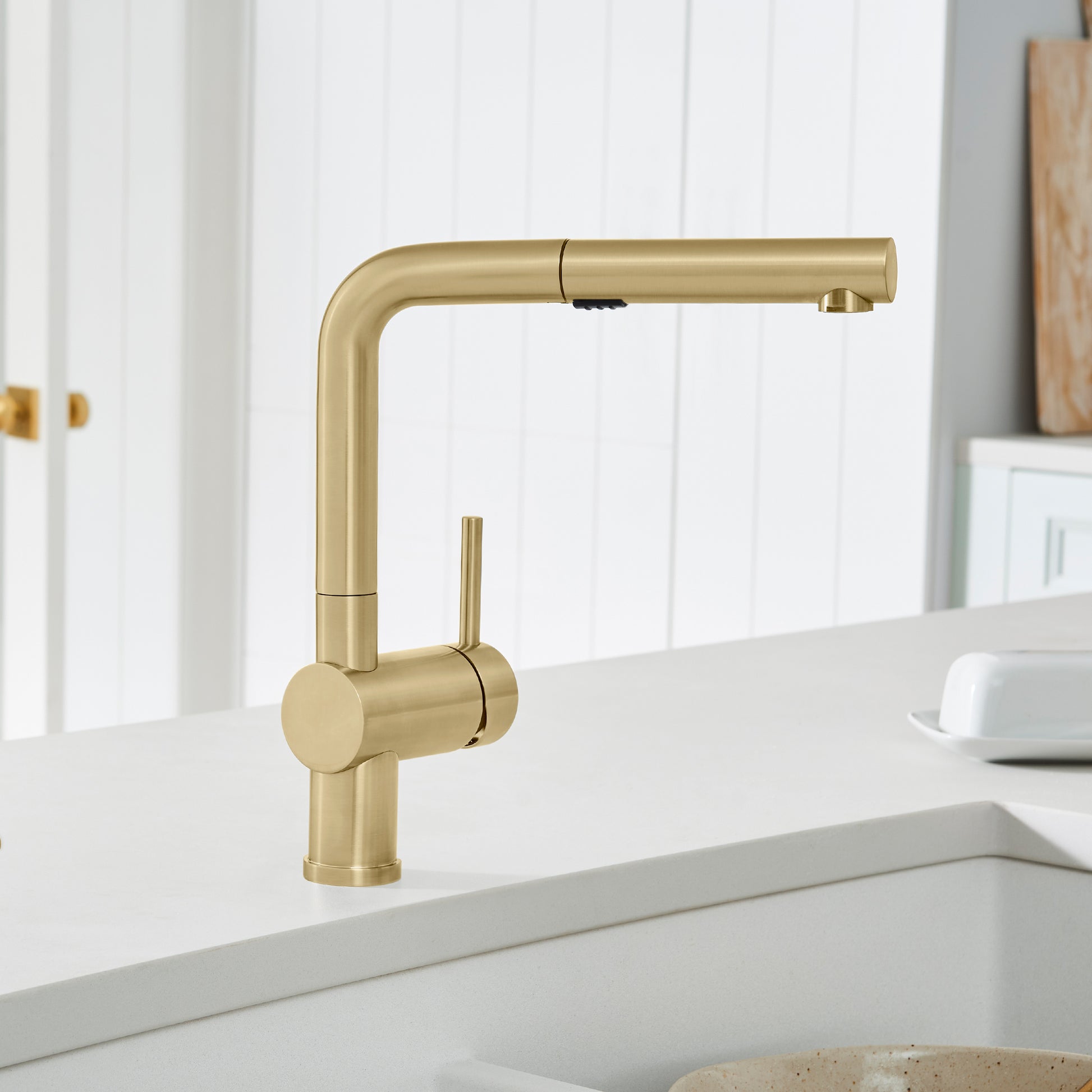 Satin gold pull-out kitchen faucet with angled spout and single lever handle mounted on white countertop.