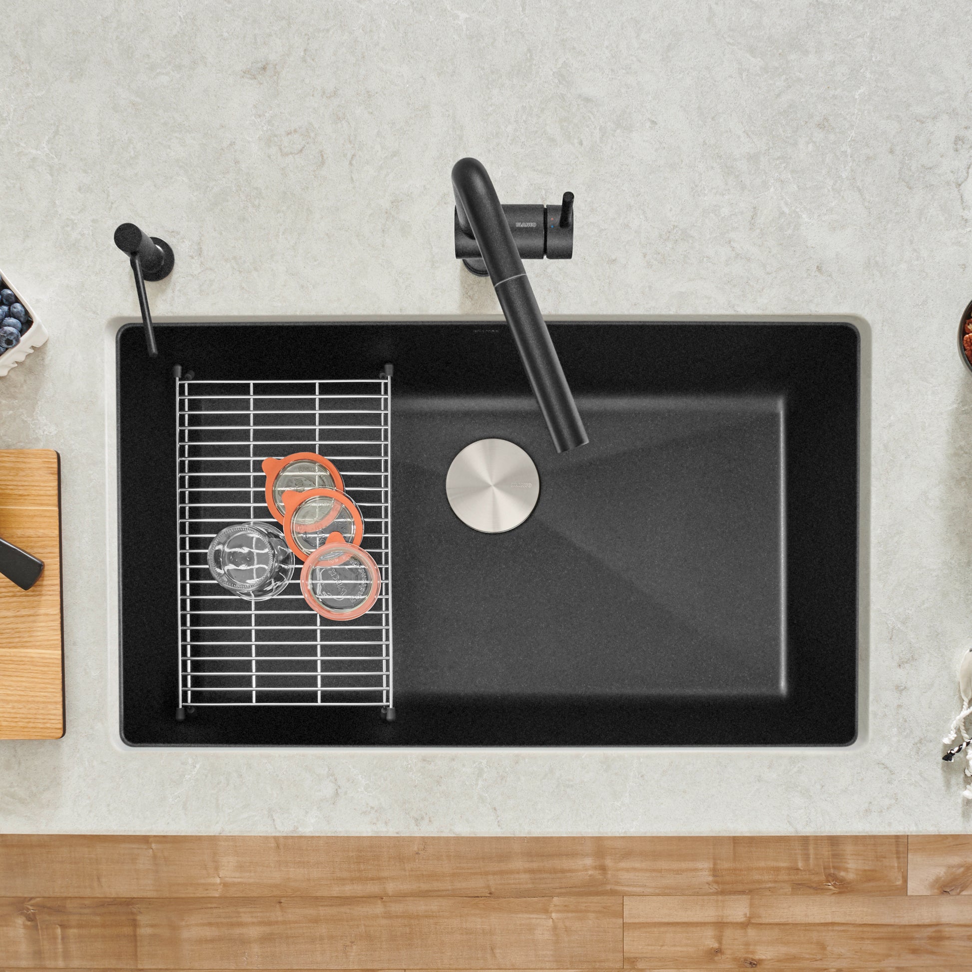 Anthracite undermount kitchen sink with single bowl, black faucet, drain cover, and metal grid insert viewed from above.