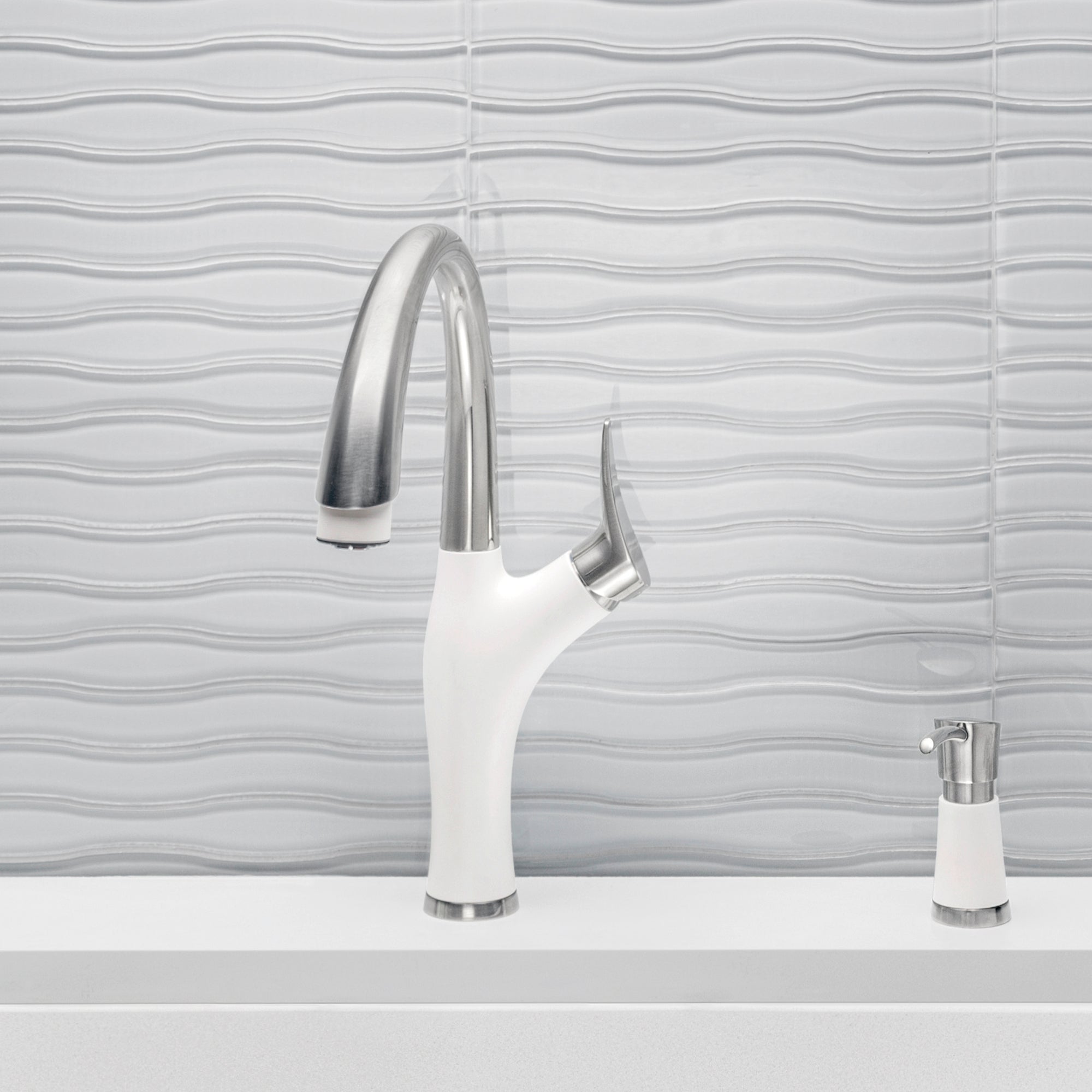 White and stainless steel pull-down kitchen faucet with curved spout and matching soap dispenser on countertop.