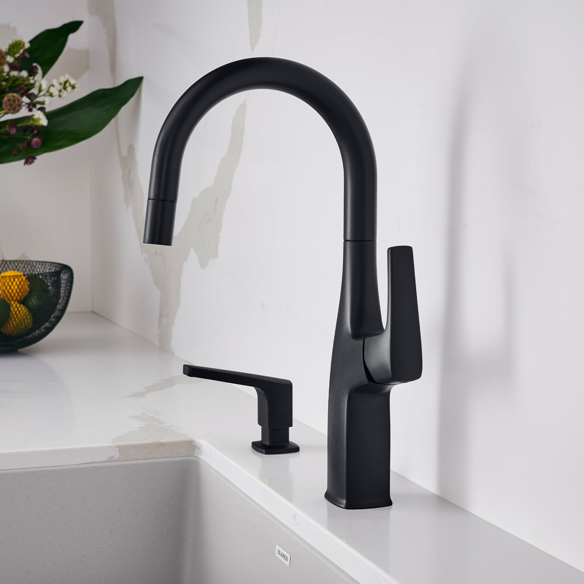 Matte black bar faucet with curved pull-down spout and lever handle mounted on white countertop beside sink.