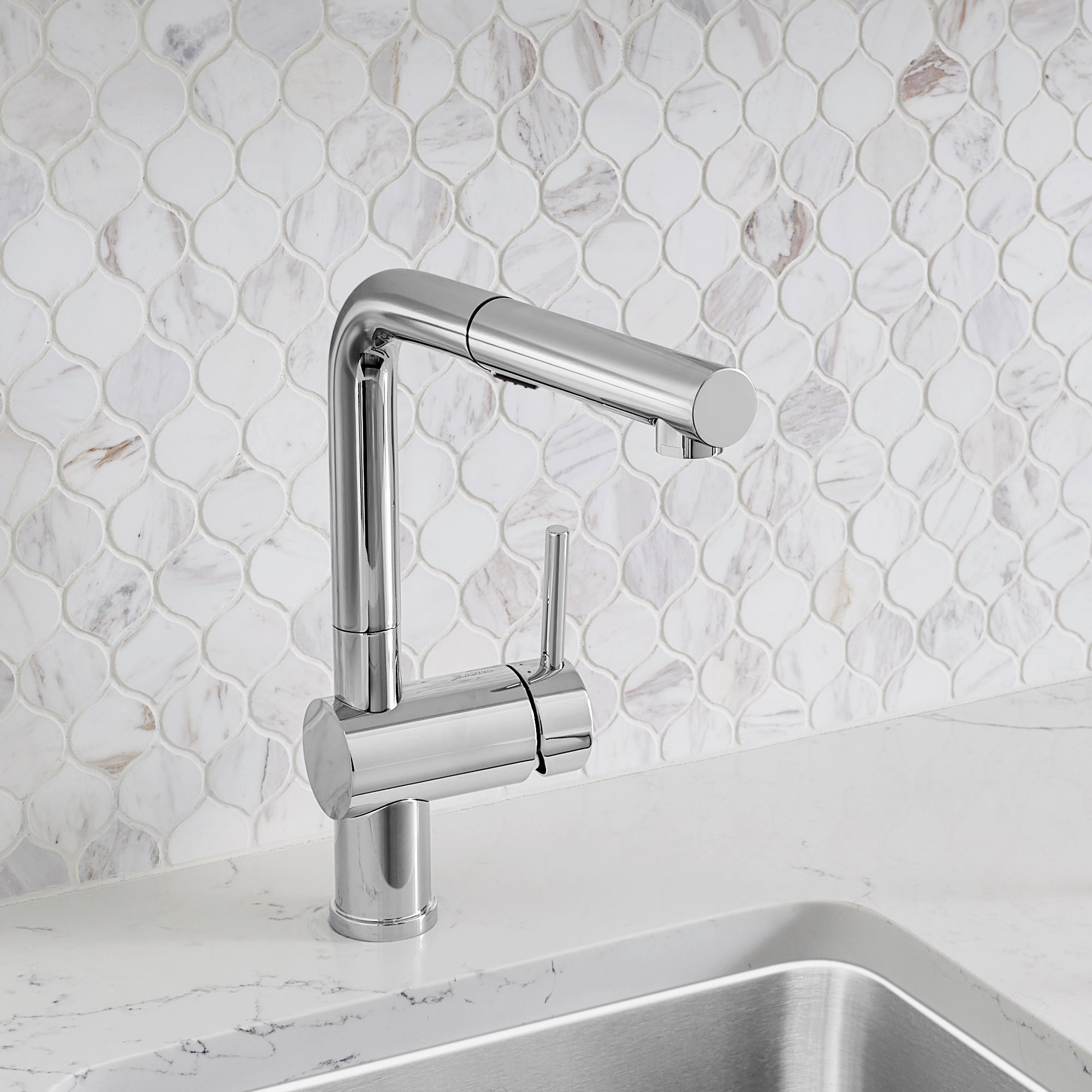 Chrome pull-out kitchen faucet with cylindrical body and extended spout over marble countertop and hexagonal tile backsplash.