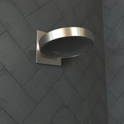 Brushed nickel round shower head with perforated face mounted on square wall connector trim against herringbone tile wall.