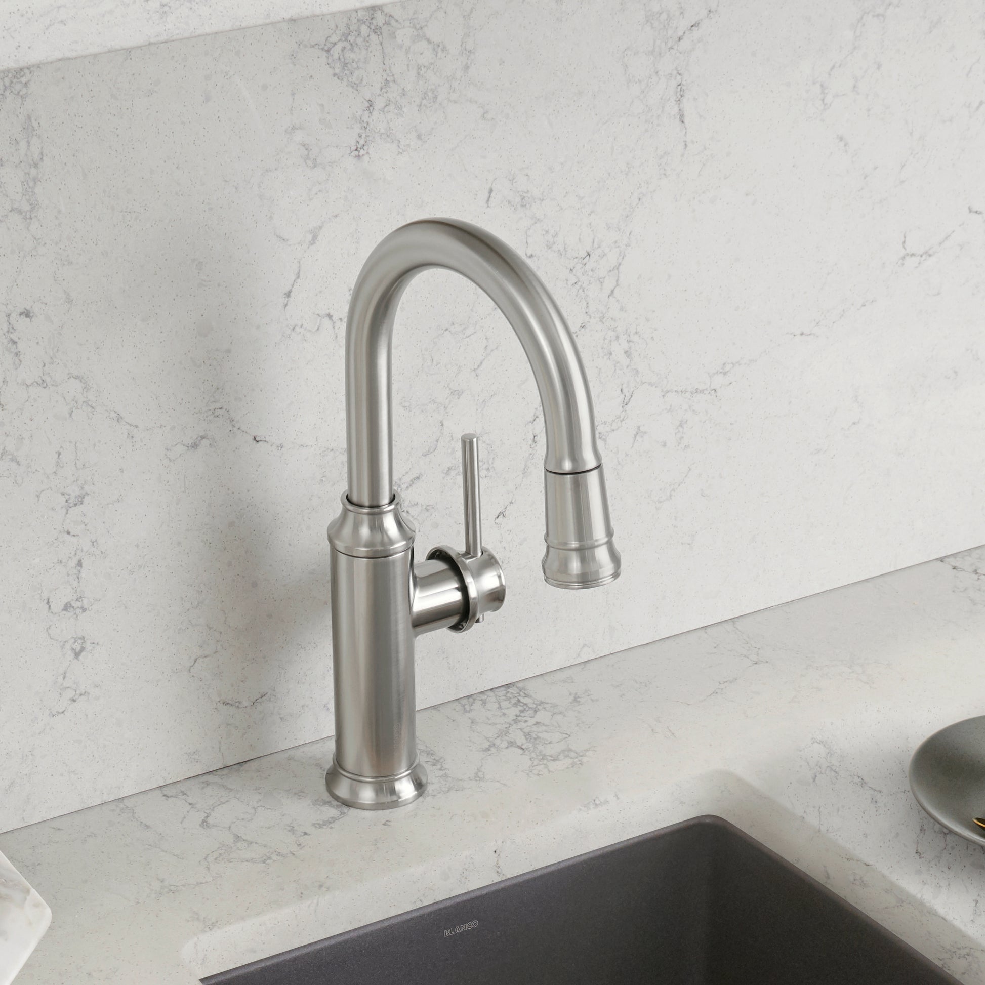 Stainless steel pull-down kitchen faucet with curved spout and side lever handle mounted on marble countertop above sink.