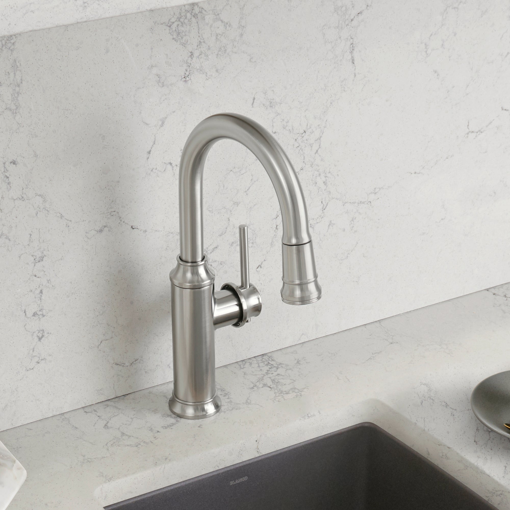 Stainless steel pull-down kitchen faucet with curved spout and side lever handle mounted on marble countertop above sink.