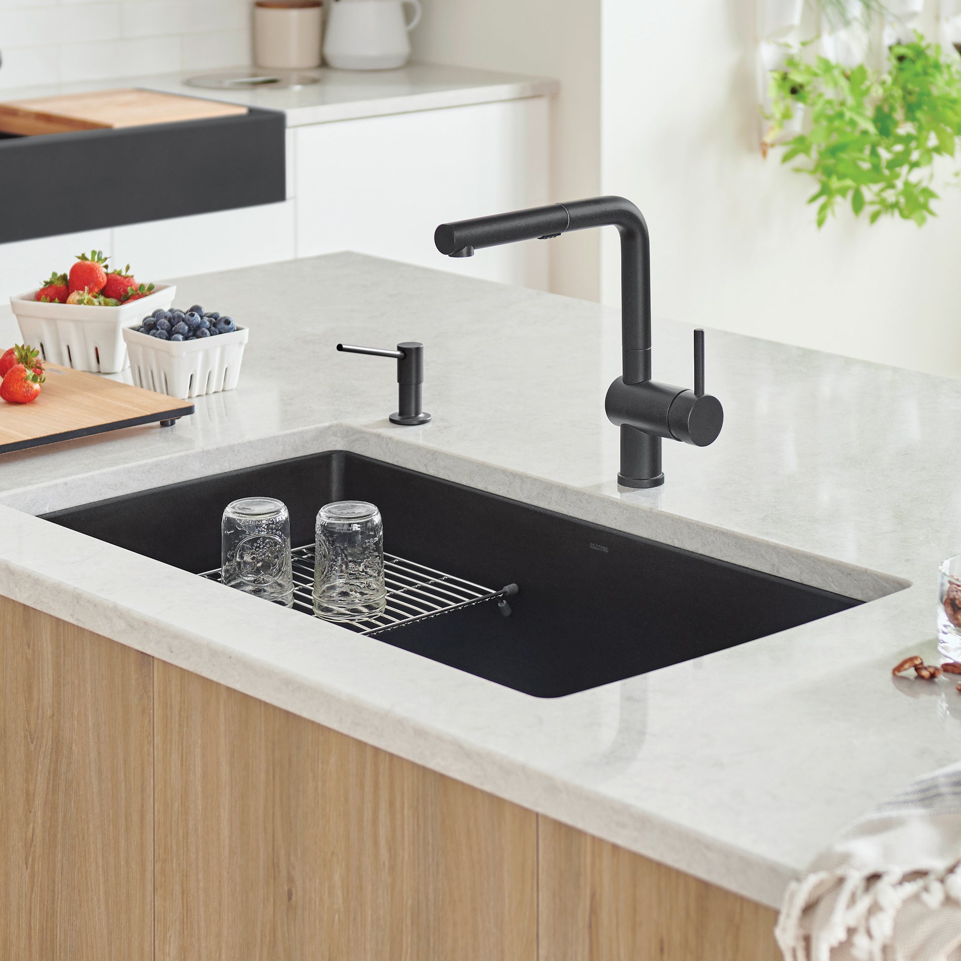 Coal black single bowl undermount kitchen sink with matching black faucet and metal strainer in countertop.