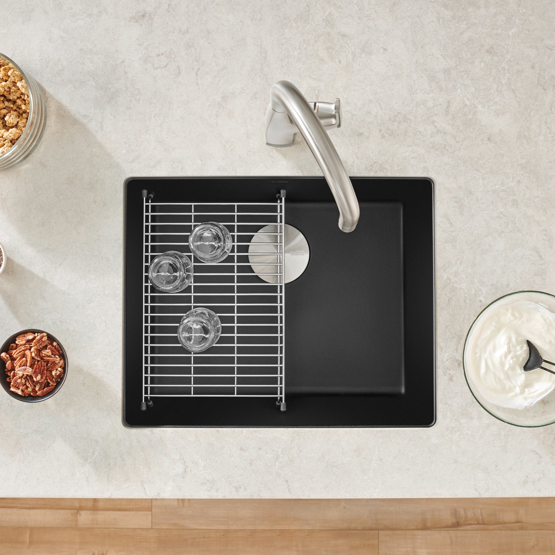 Coal black single-bowl kitchen sink with stainless steel faucet, metal grid insert, and drainboard, viewed from above.