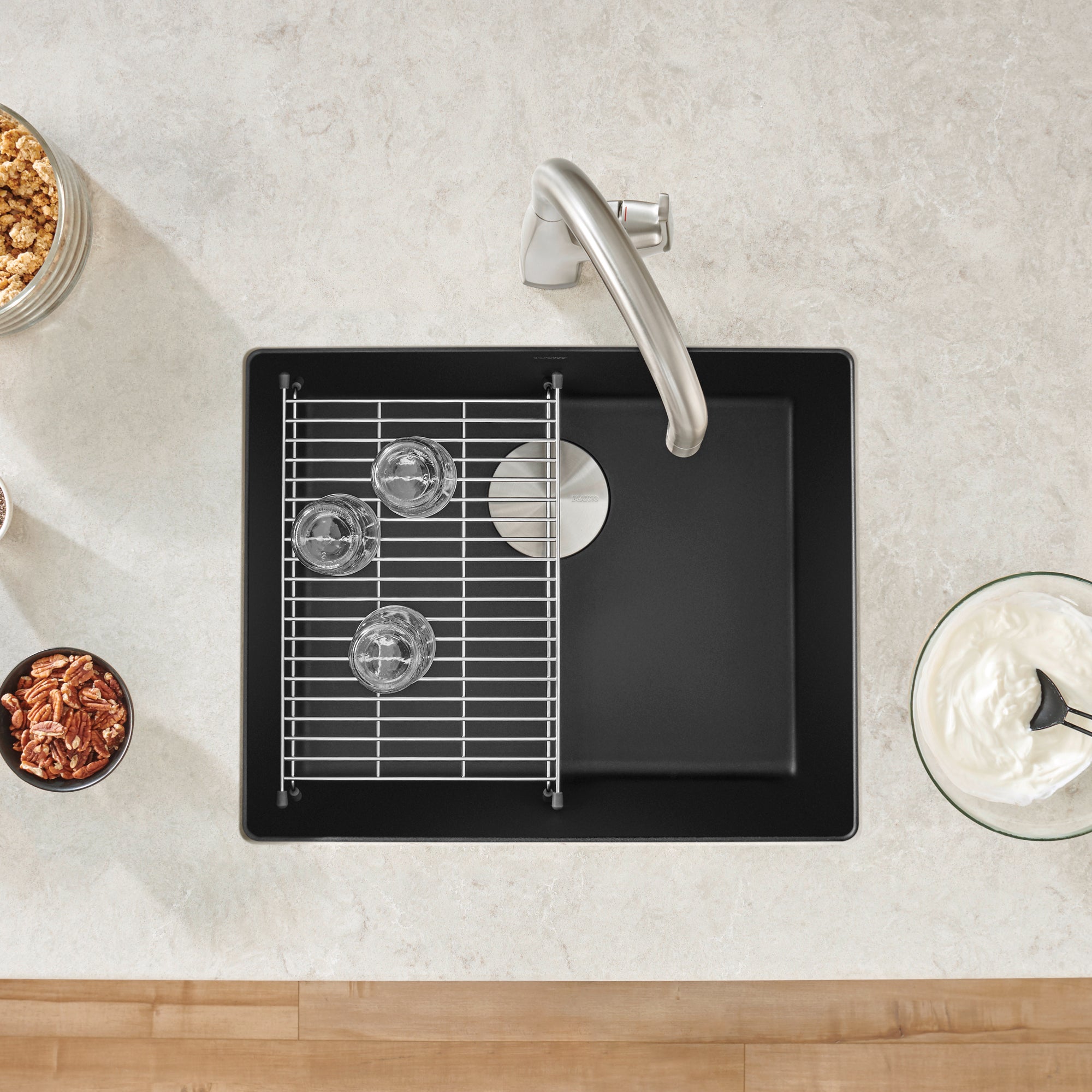 Coal black single-bowl kitchen sink with stainless steel faucet, metal grid insert, and drainboard, viewed from above.