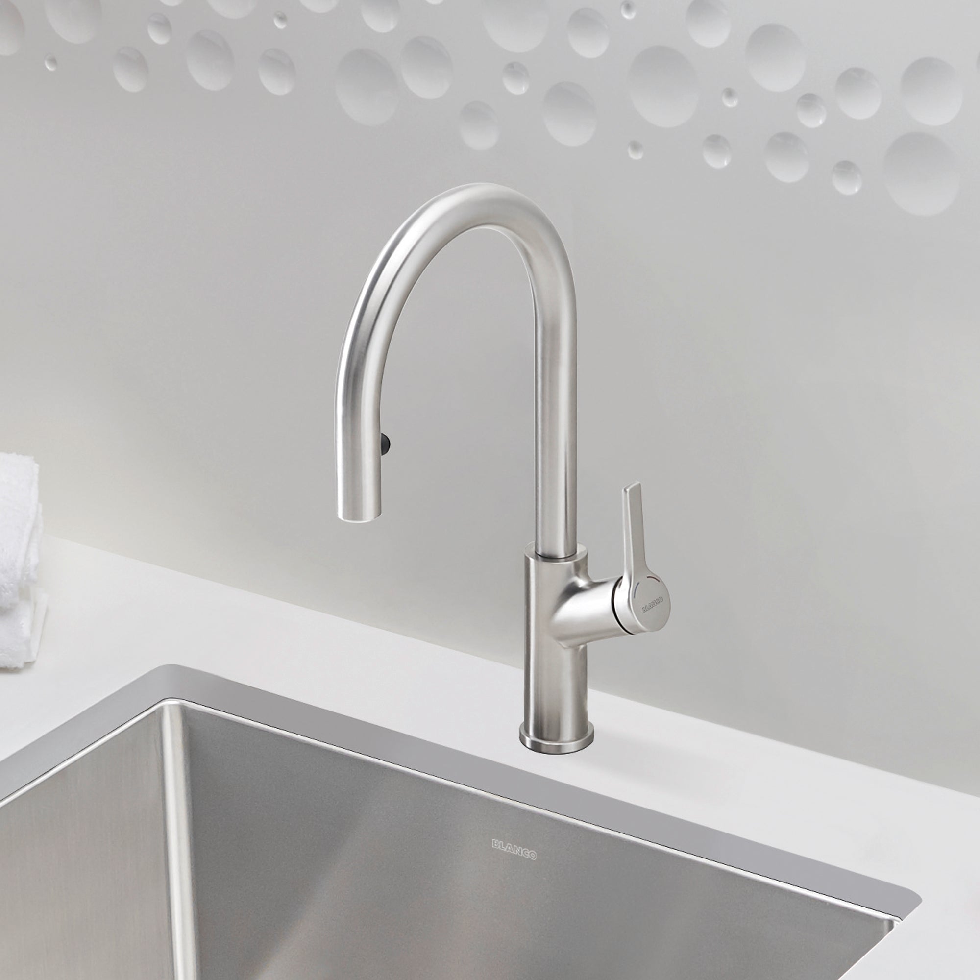 Stainless steel pull-down kitchen faucet with curved spout and single lever handle mounted above undermount sink.