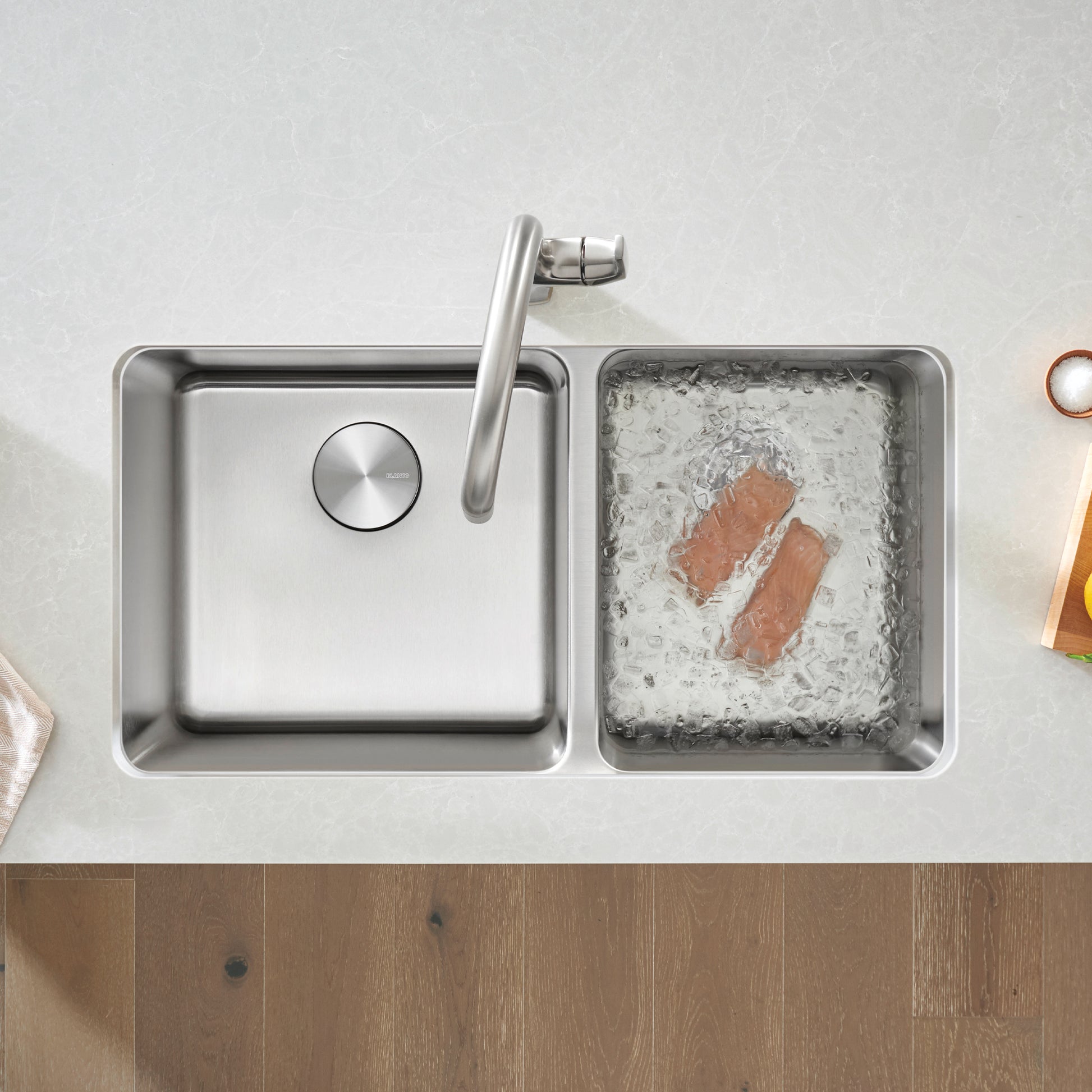 Stainless steel double bowl undermount sink with larger left basin, smaller right basin containing ice and fish, chrome fauce
