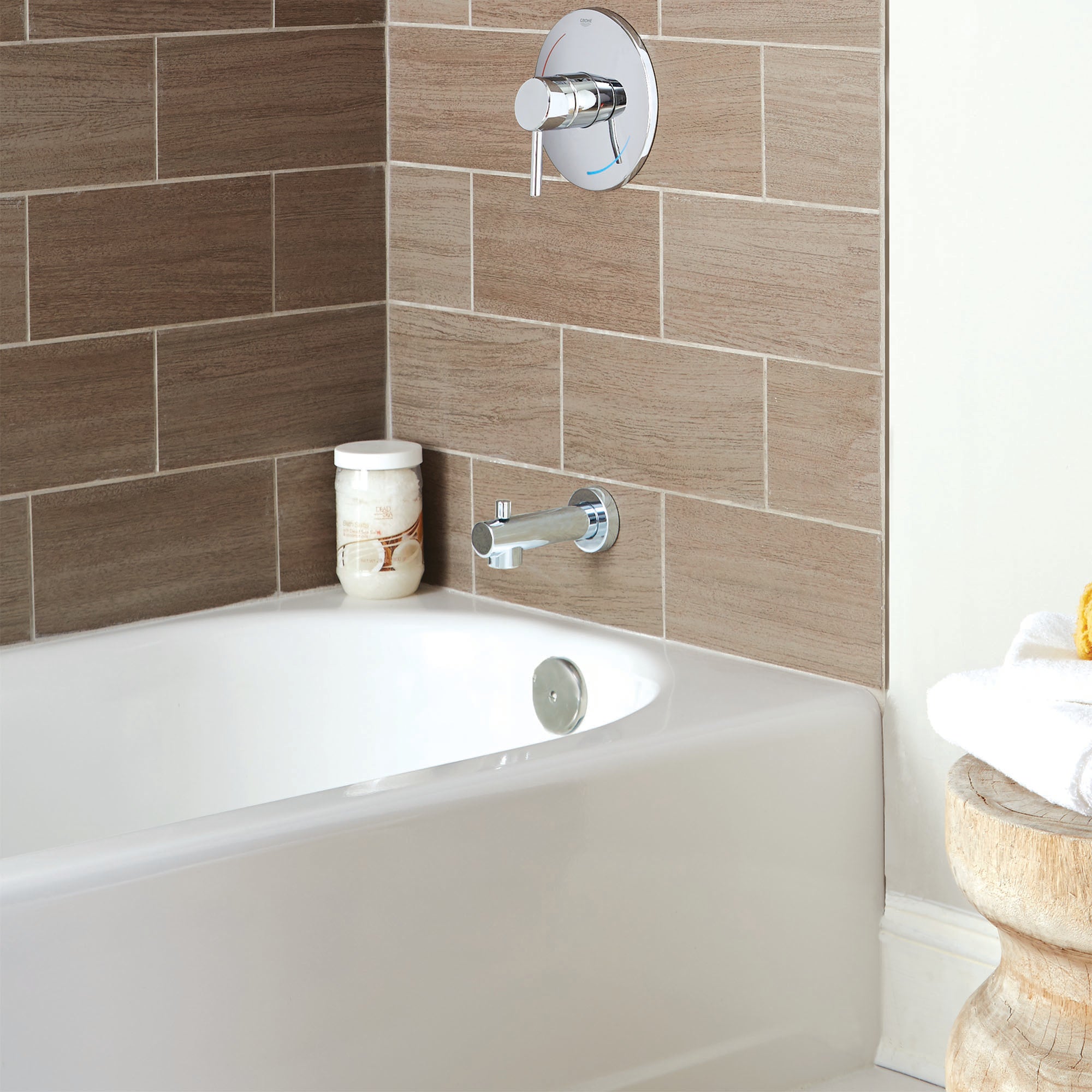 Chrome diverter tub spout with round trim plate and single lever handle mounted on tile wall above bathtub.