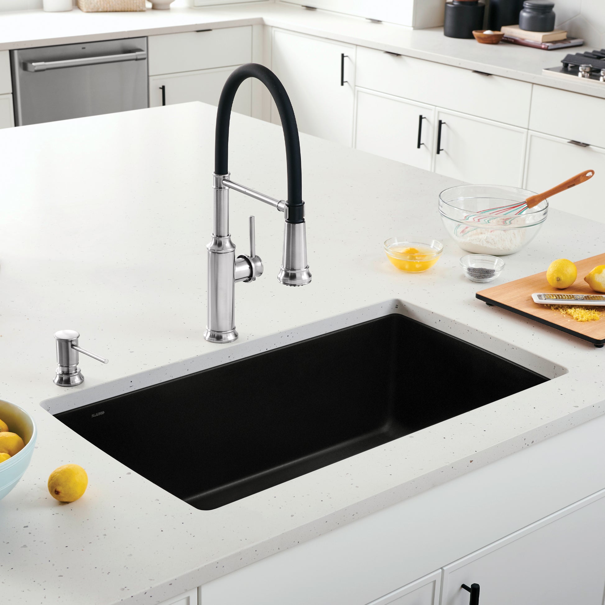 Coal black single bowl undermount kitchen sink with chrome pull-down faucet and soap dispenser in white countertop.
