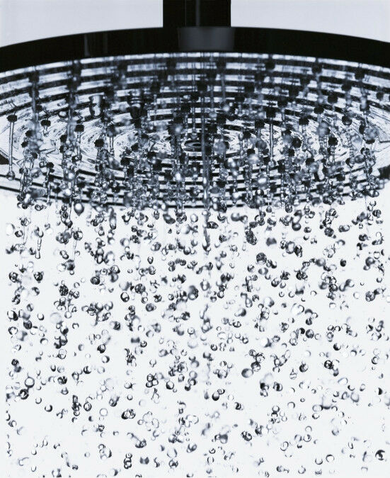 Chrome shower head with perforated face spraying water droplets downward in multiple streams.