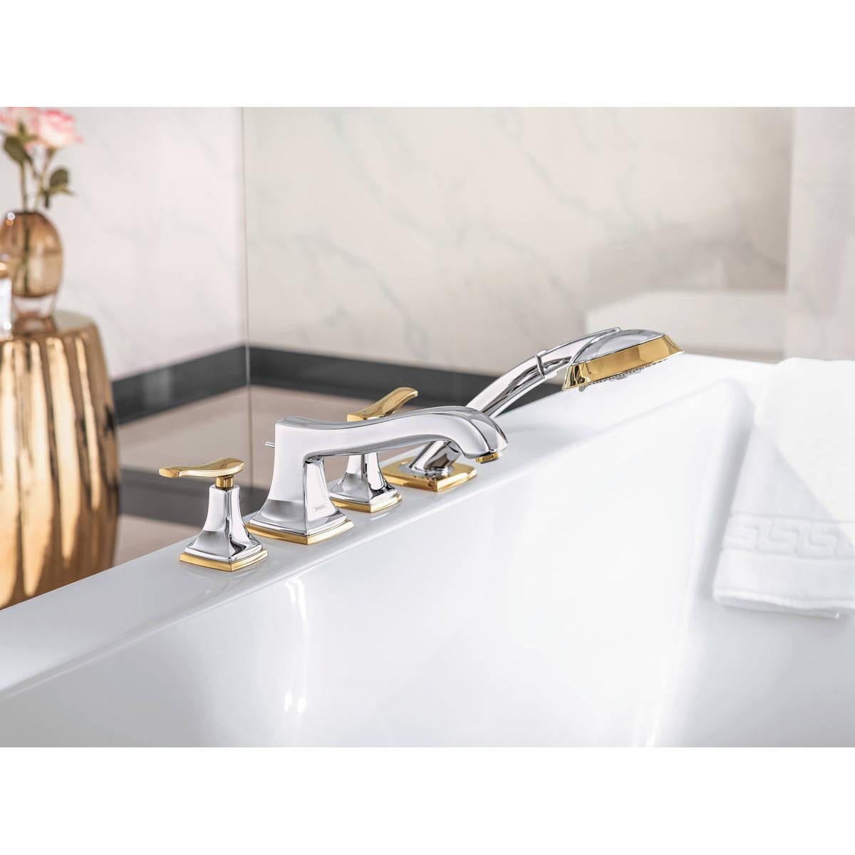 Chrome and gold-tone four-hole tub faucet trim set with lever handles and handheld showerhead mounted on white bathtub rim.