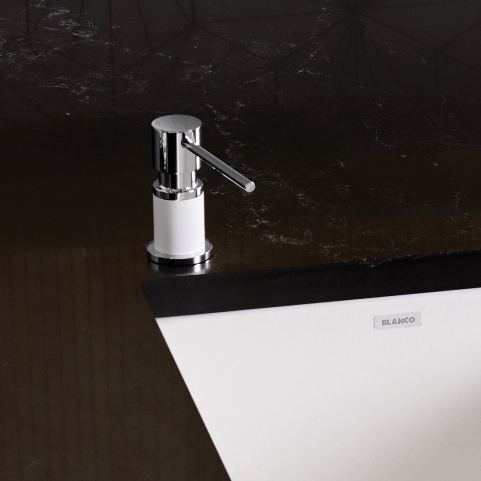 Chrome and white countertop soap dispenser with cylindrical pump lever mounted on dark marble surface.