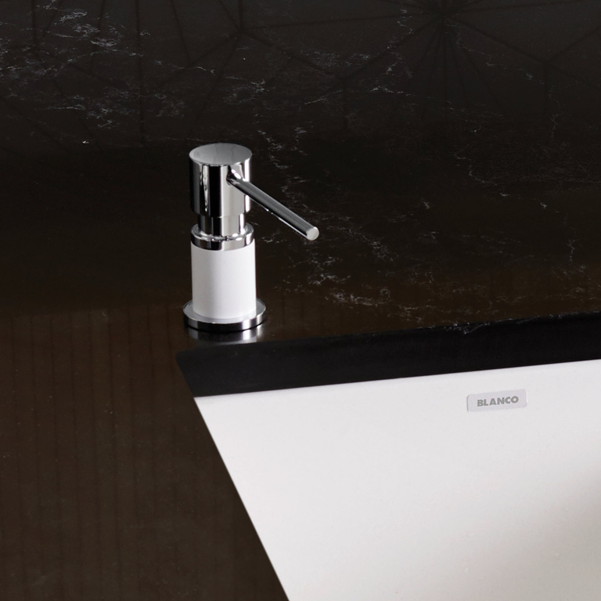 Chrome and white countertop soap dispenser with cylindrical pump lever mounted on dark marble surface.