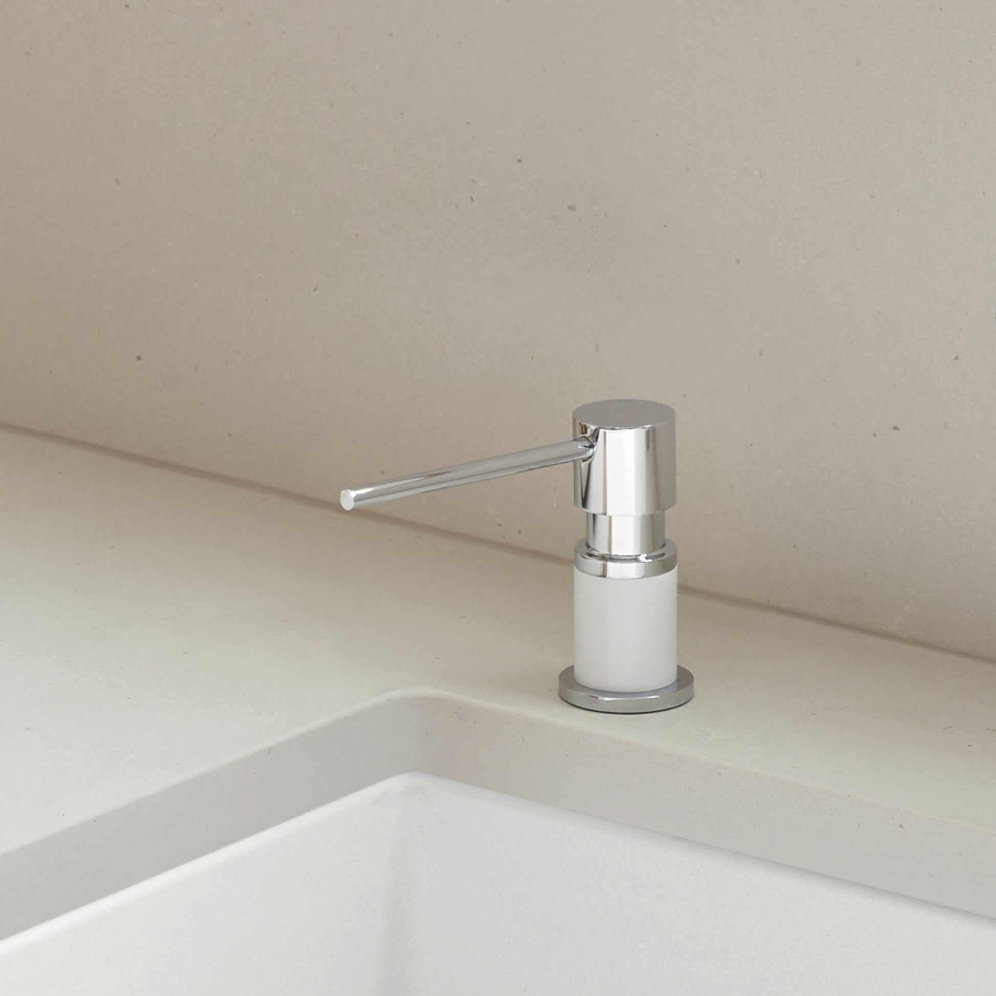 Chrome and white soap dispenser mounted on white countertop next to sink.