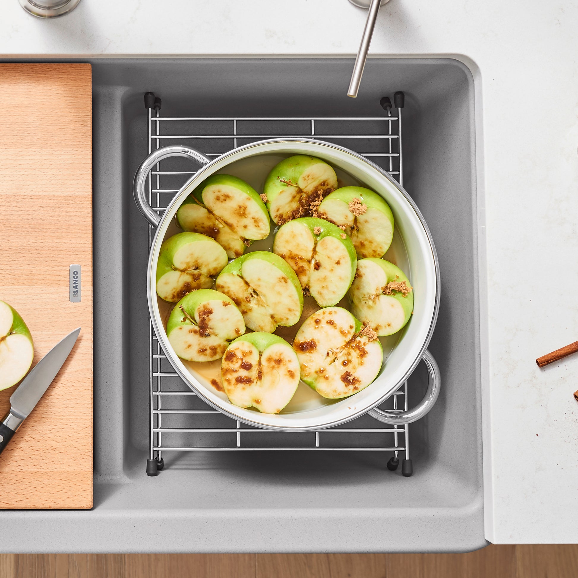 Stainless steel sink grid with rectangular design and black handles, positioned in gray sink basin holding round bowl of slic
