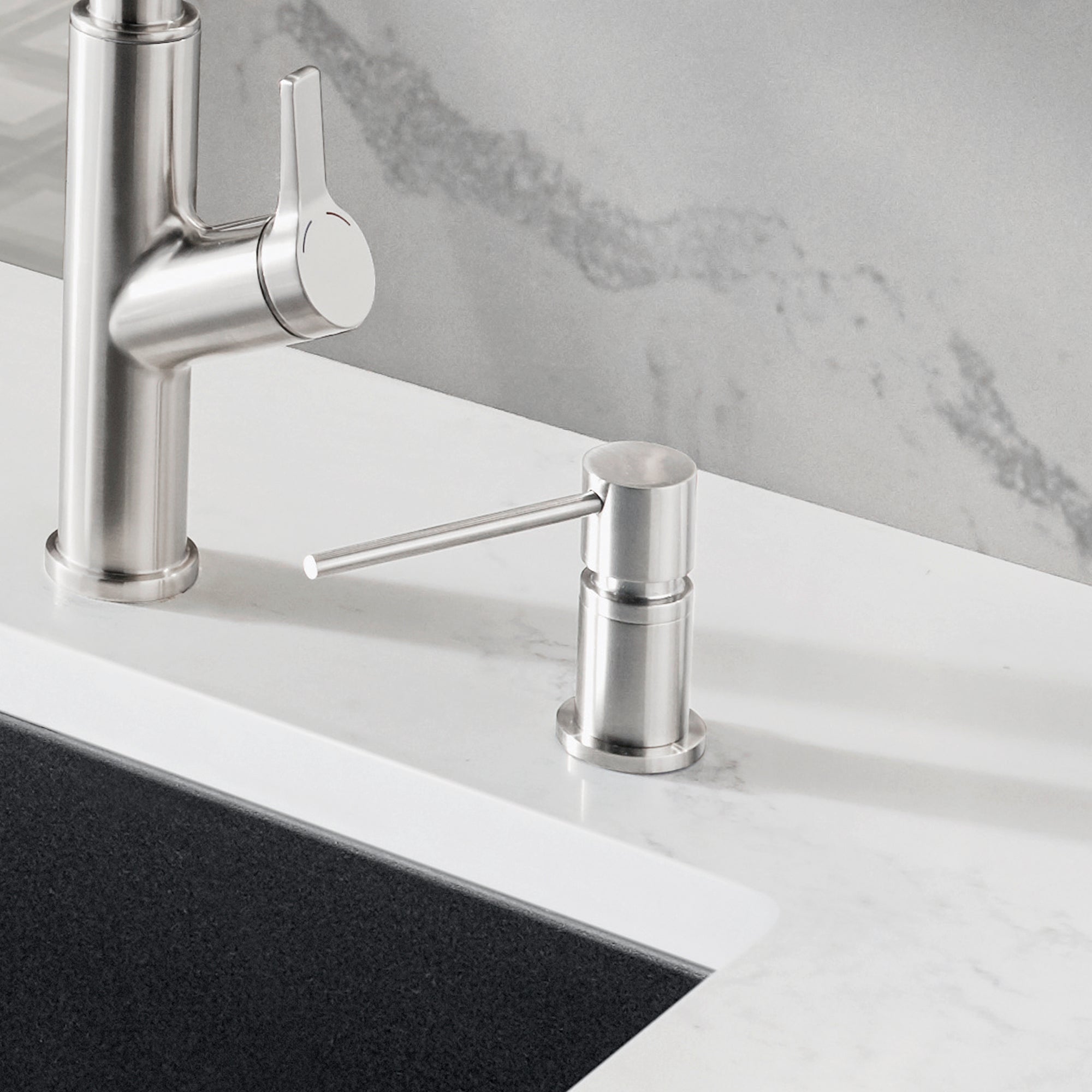 Stainless steel soap dispenser with cylindrical body and round pump lever, positioned next to a kitchen faucet on white count