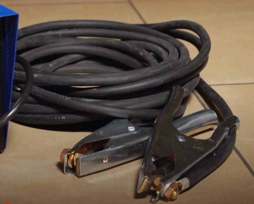 Two black cables with metal lugs and pipe clamps attached at the ends, coiled together.