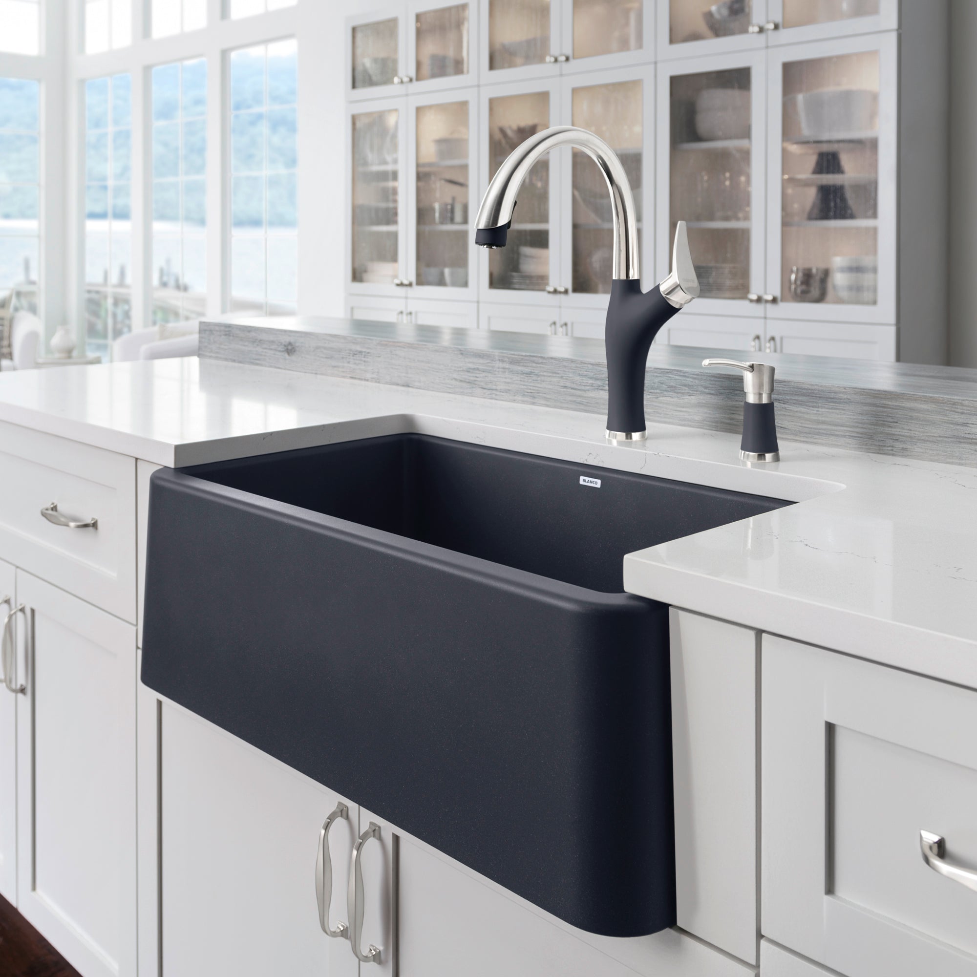 Anthracite apron front kitchen sink with curved edges and black pull-down faucet installed in white countertop.