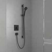 Matte black wall-mounted shower set with square valve trim, handheld showerhead on rail, and body jet mounted on tile wall.