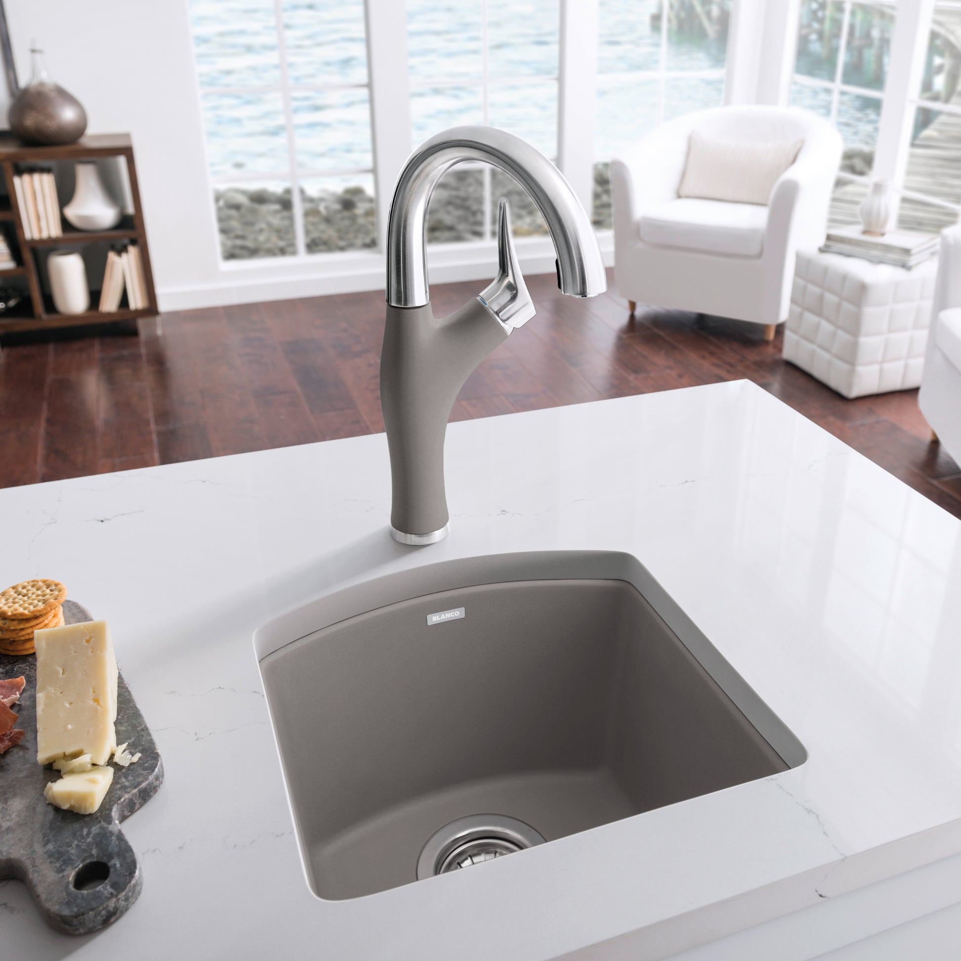 Truffle-colored composite bar sink with curved edges installed in white countertop, paired with chrome pulldown faucet.