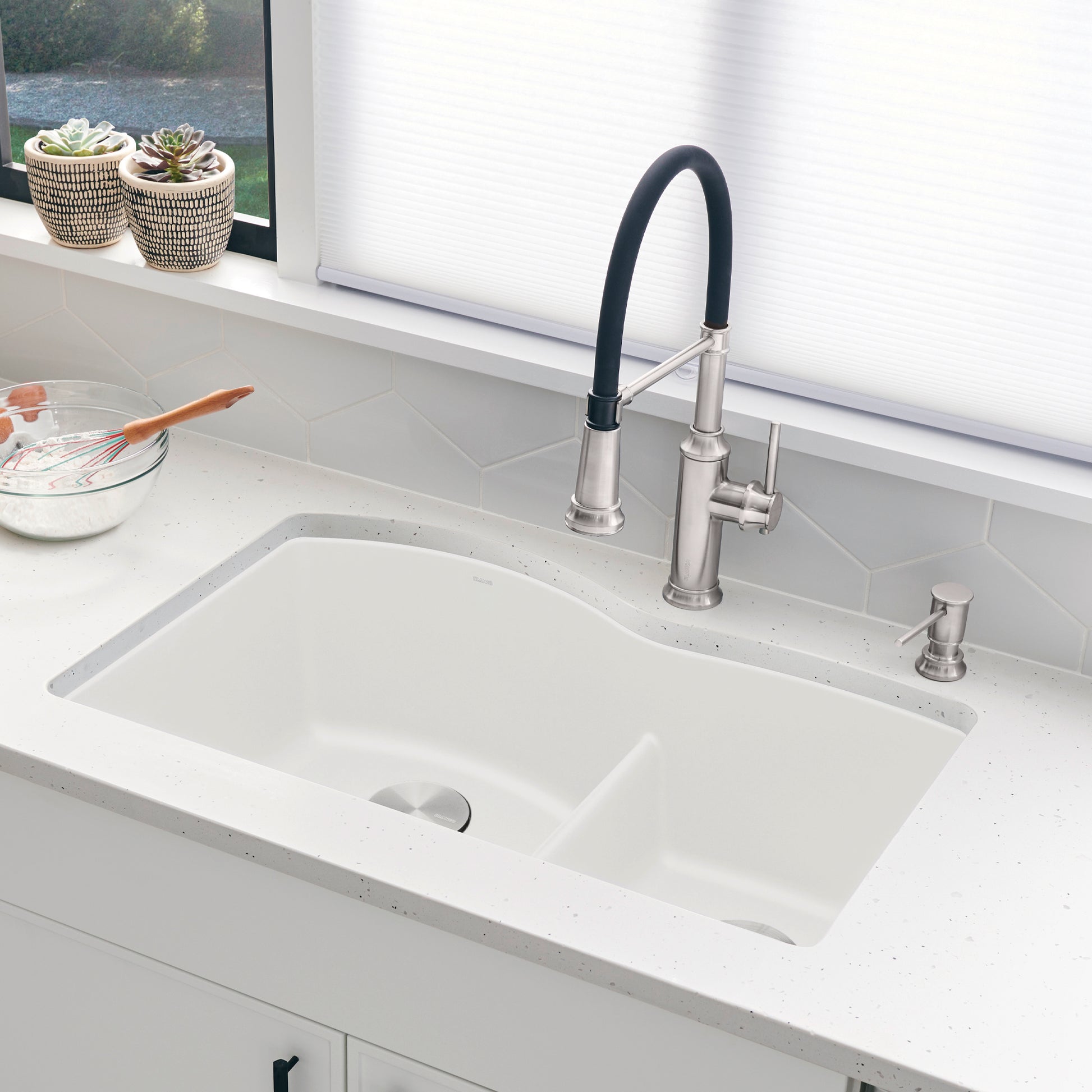 White rectangular undermount kitchen sink with low divide and stainless steel faucet with black handle.