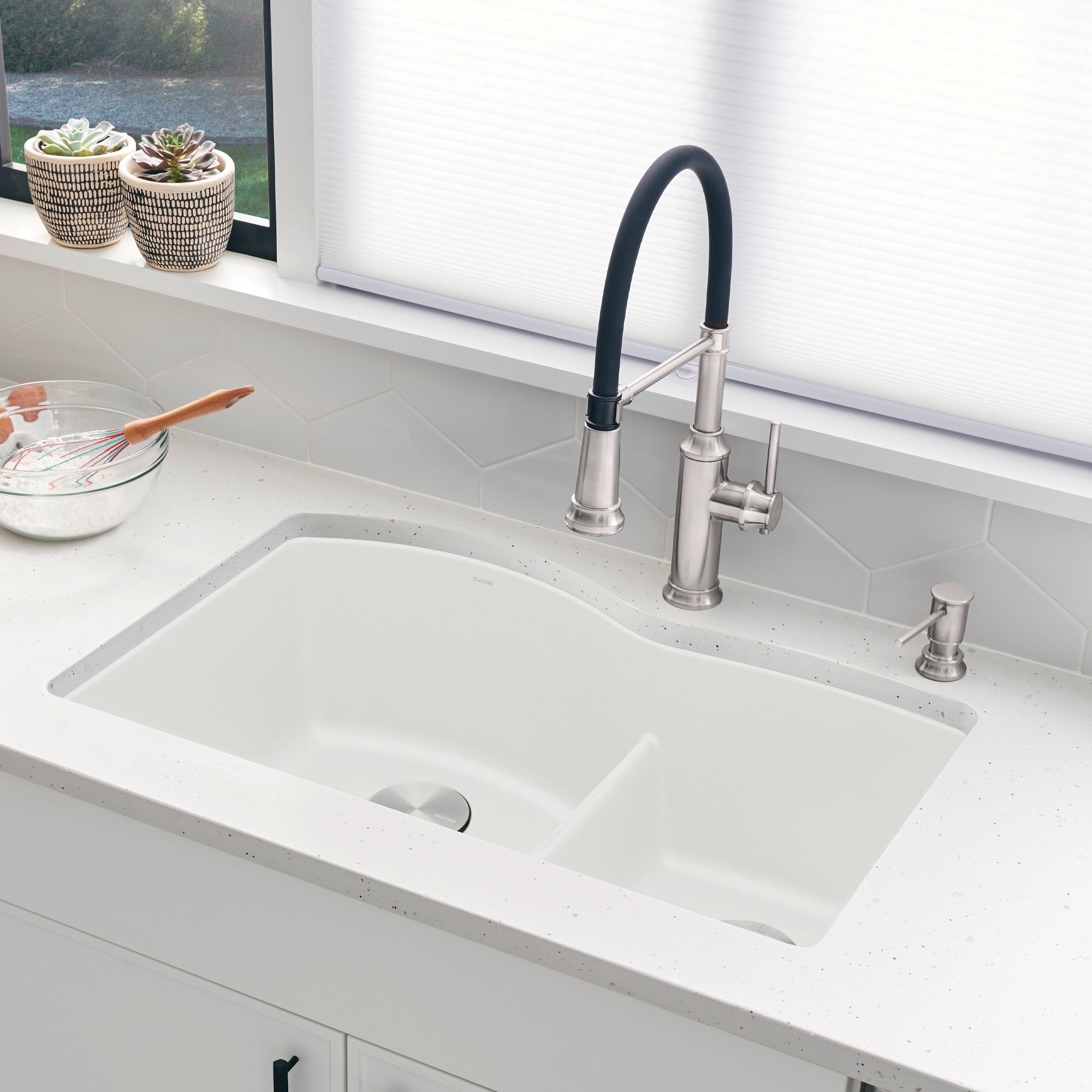 White rectangular undermount kitchen sink with low divide and stainless steel faucet with black handle.