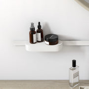 Matte white wall-mounted storage basket with cover holding brown glass bottles and a dark container.