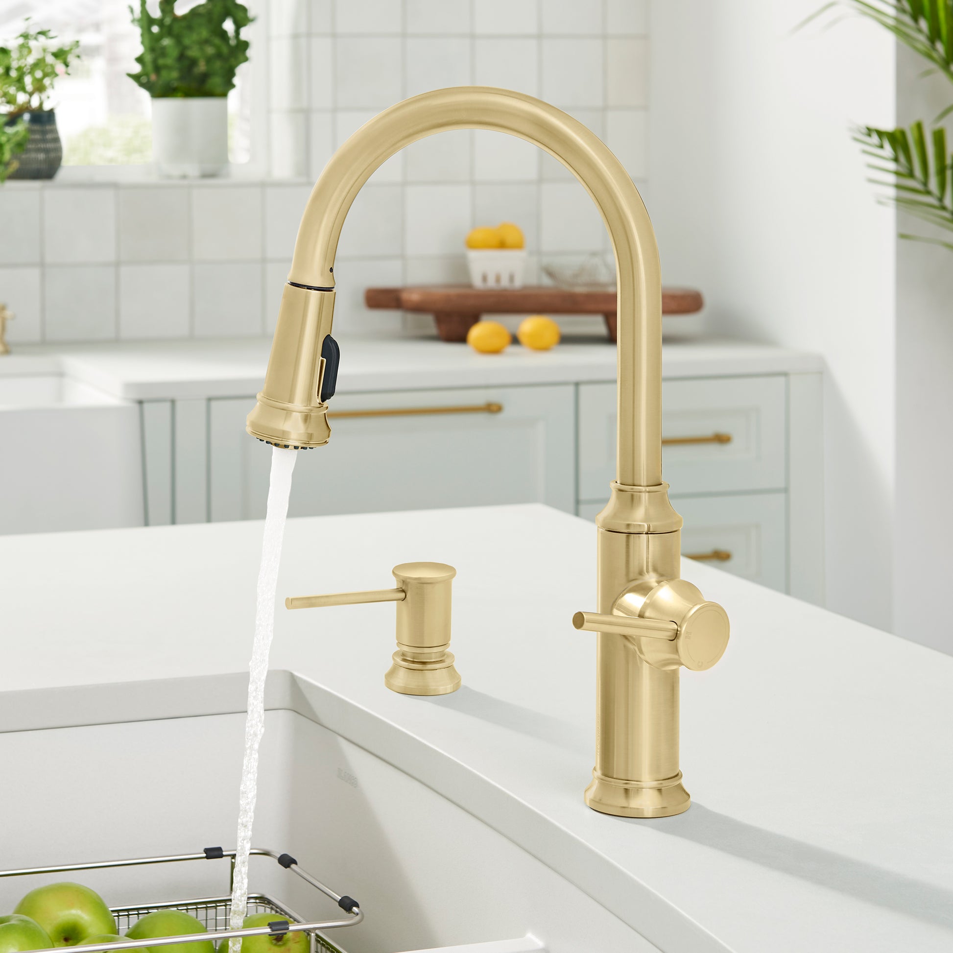 Satin gold pull-down kitchen faucet with high arching spout and matching soap dispenser installed on white sink.