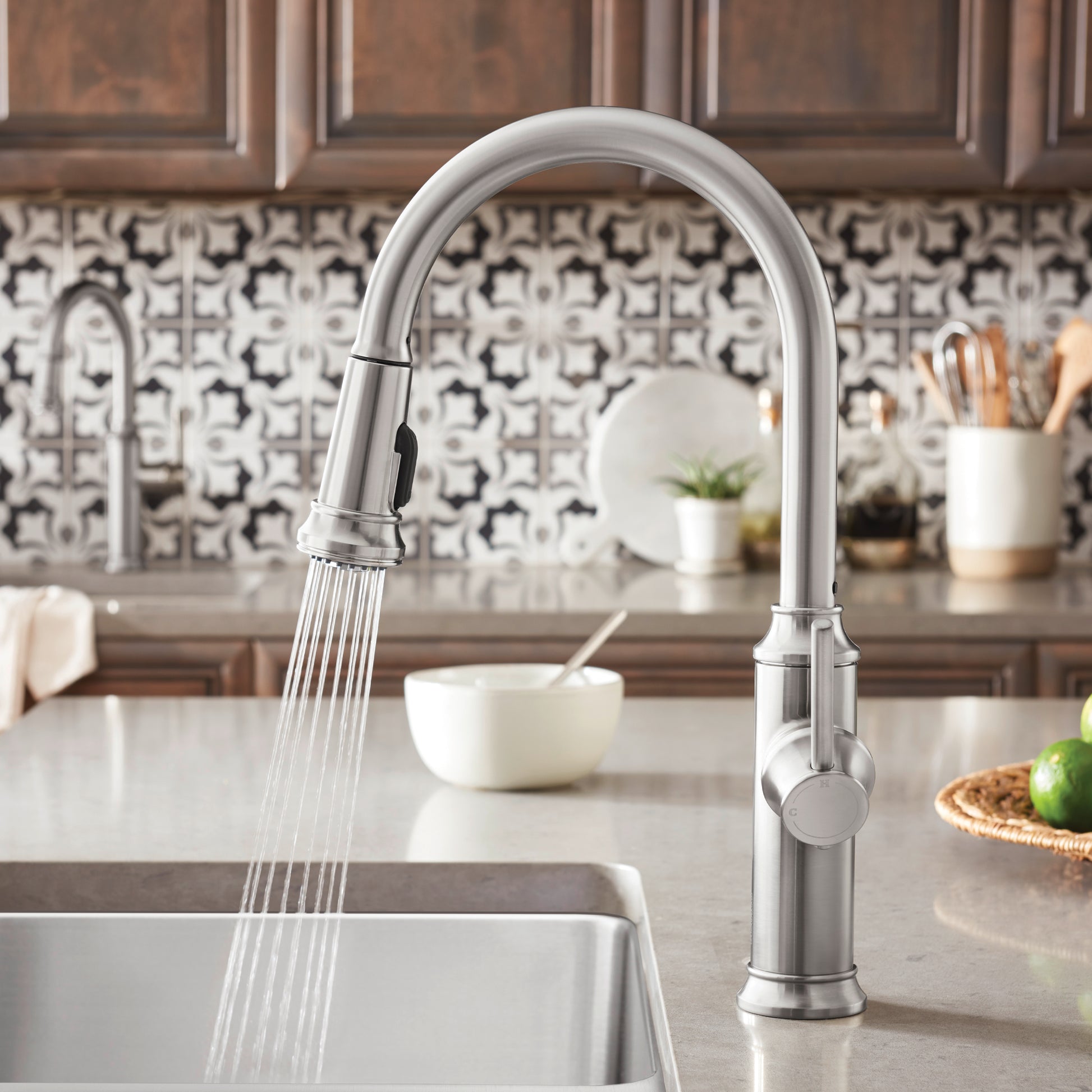 Stainless steel pull-down kitchen faucet with arched spout and spray head extended over white sink.