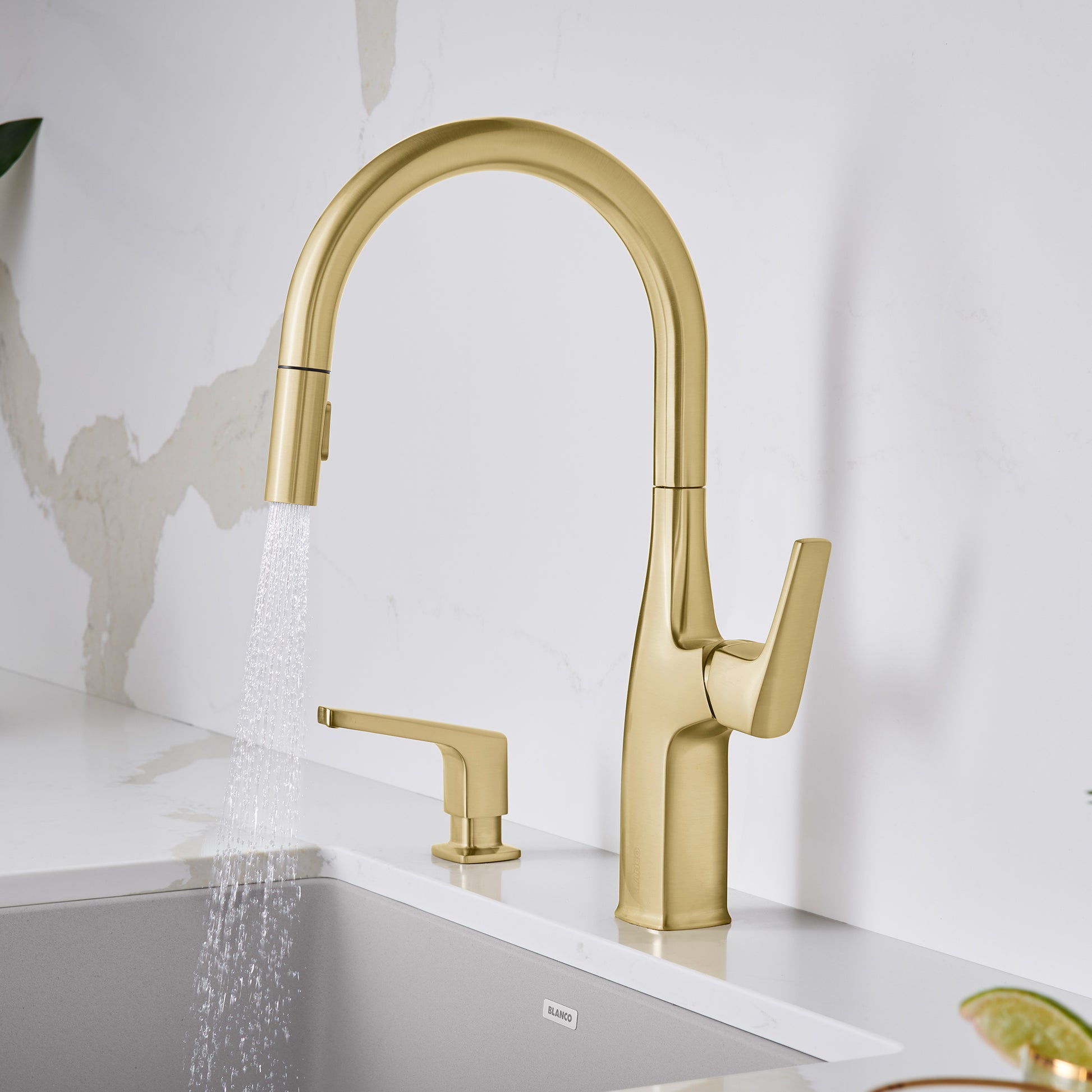 Satin gold pull-down kitchen faucet with tall arched spout, single lever handle, and matching soap dispenser on white sink co