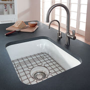 White fireclay undermount sink with rounded rectangular shape, stainless steel faucet, and grid insert on dark countertop.