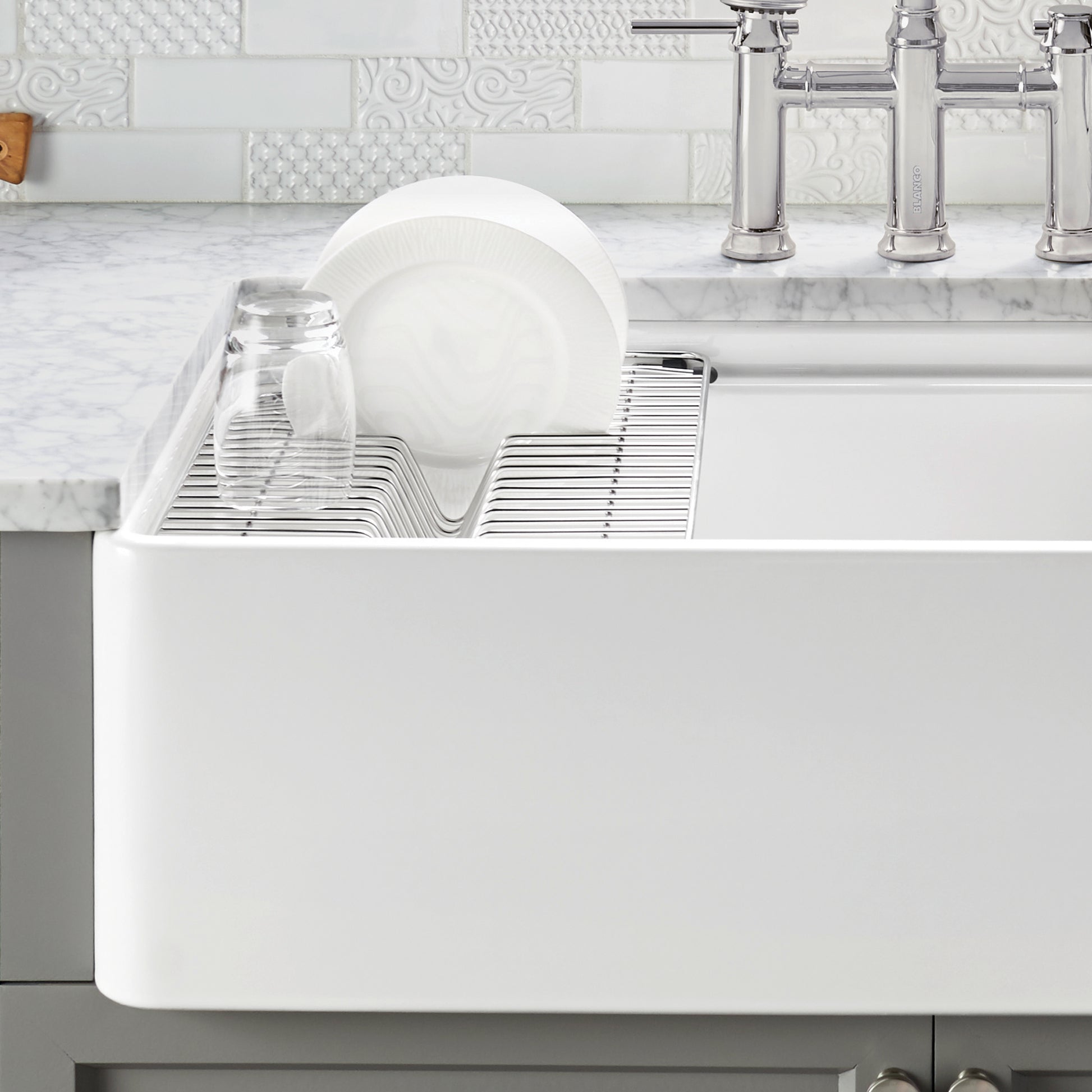 Stainless steel dish rack with plate slot and cup holders installed in white apron front sink.
