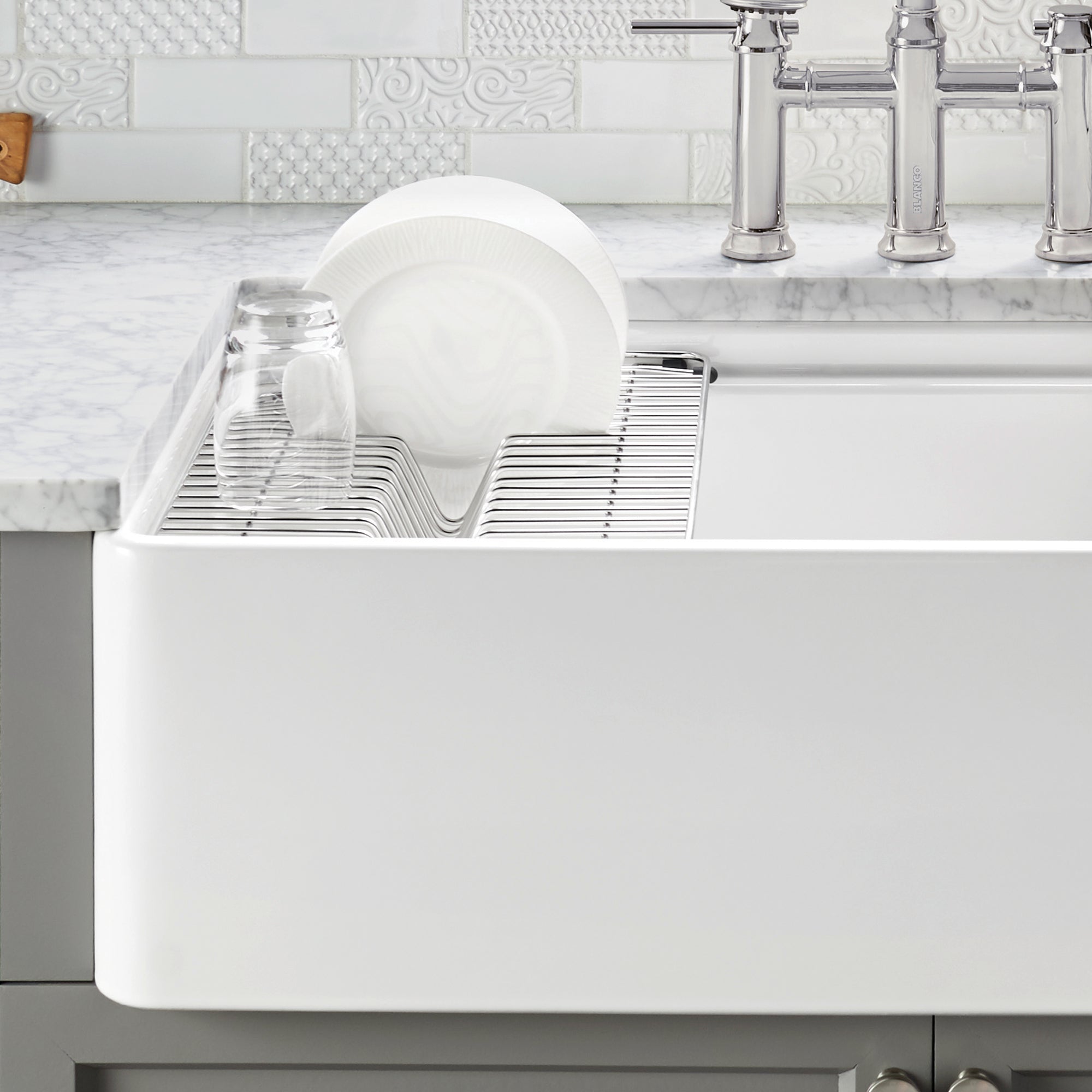 Stainless steel dish rack with plate slot and cup holders installed in white apron front sink.