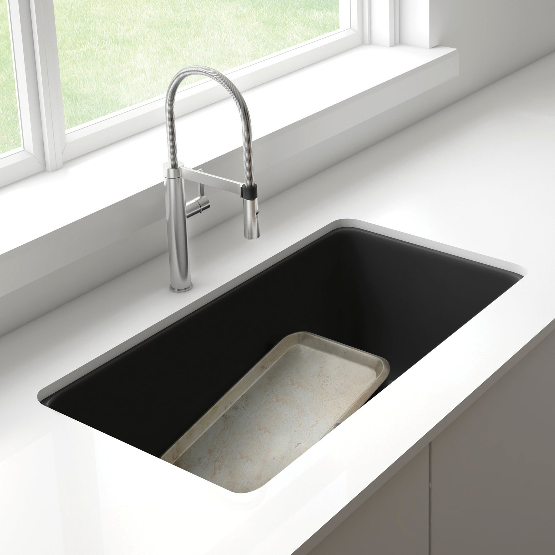 Anthracite undermount kitchen sink with low divider and stainless steel pull-down faucet installed in white countertop.