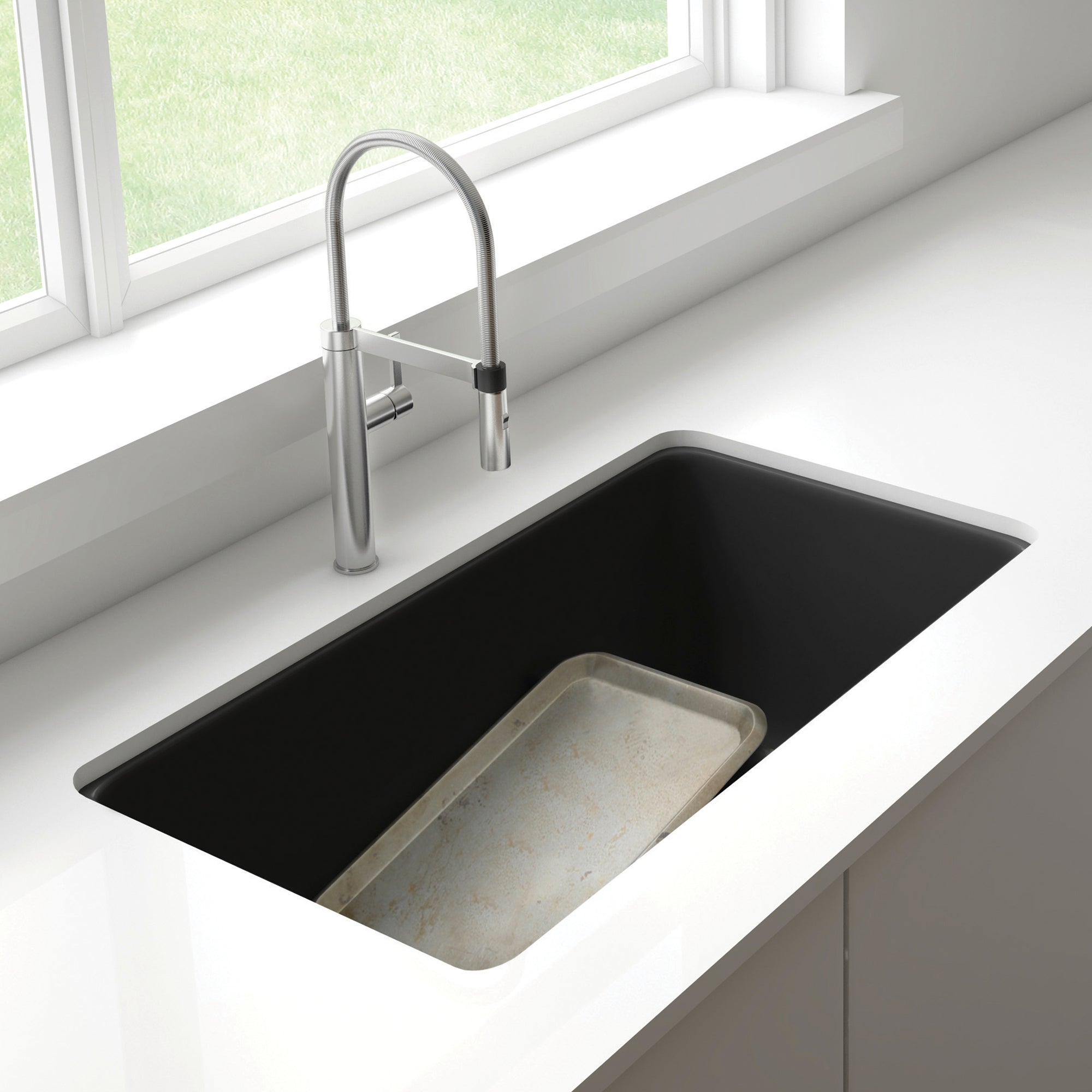 Anthracite undermount kitchen sink with low divider and stainless steel pull-down faucet installed in white countertop.
