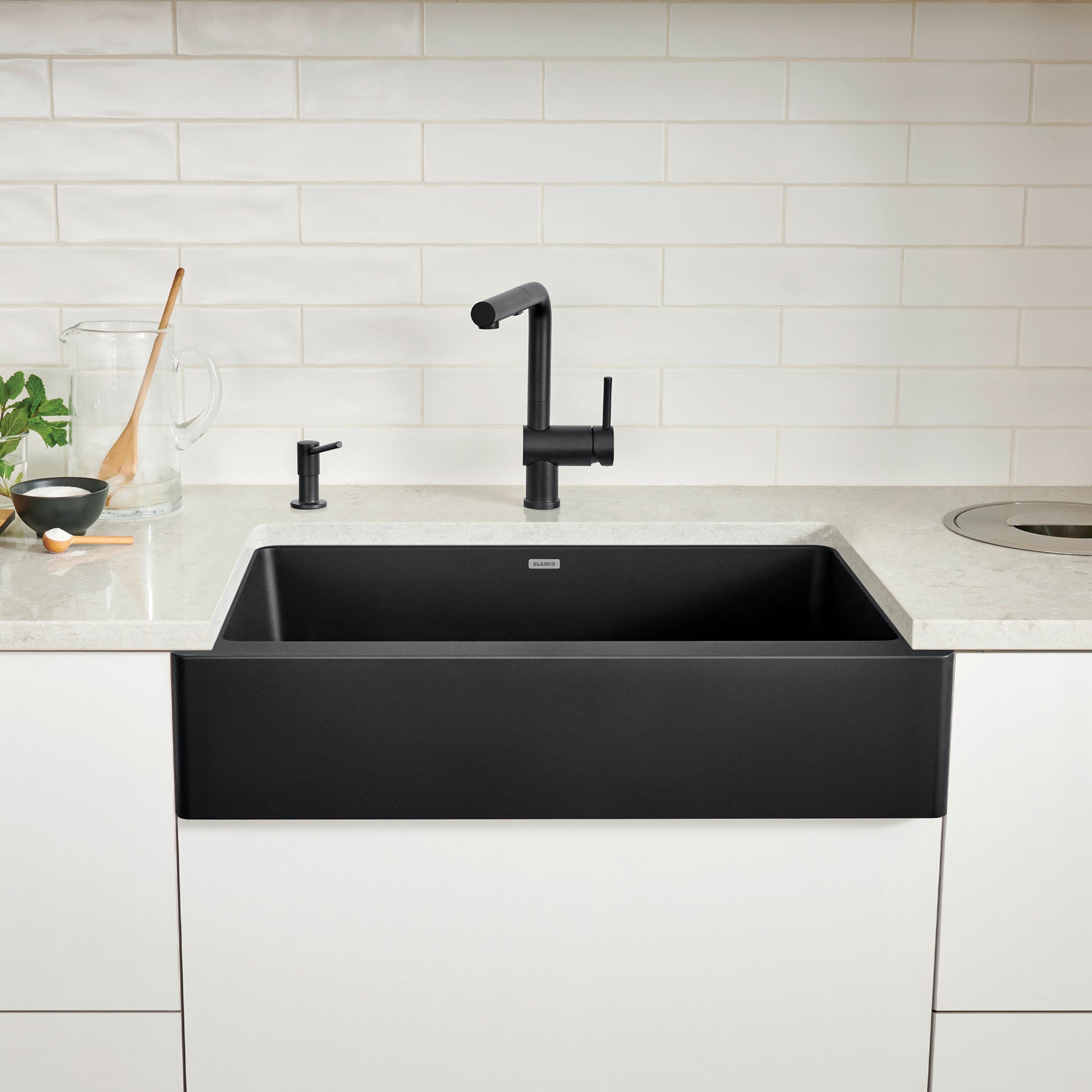 Coal black farmhouse apron sink with single basin installed in white countertop with black faucet.