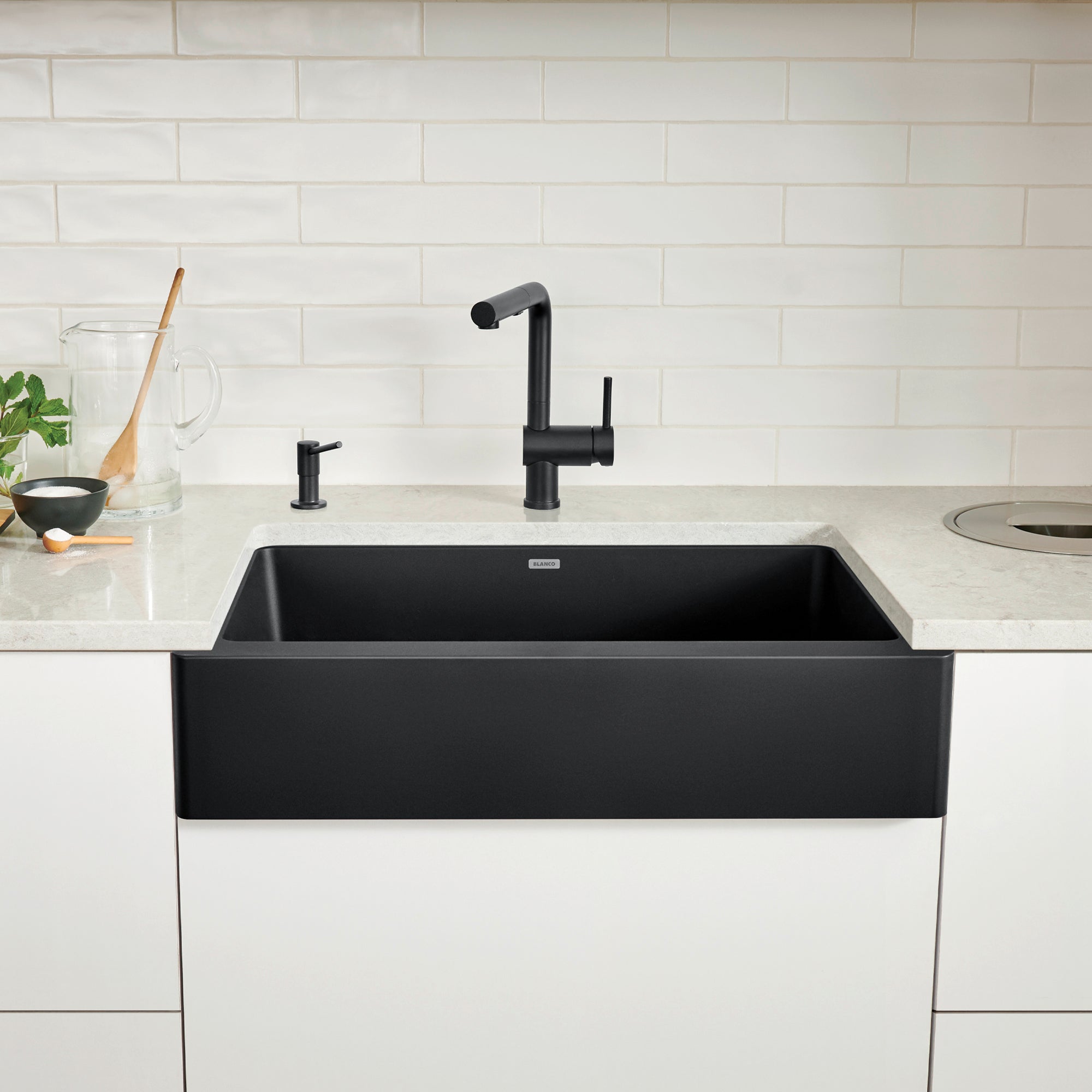Coal black farmhouse apron sink with single basin installed in white countertop with black faucet.