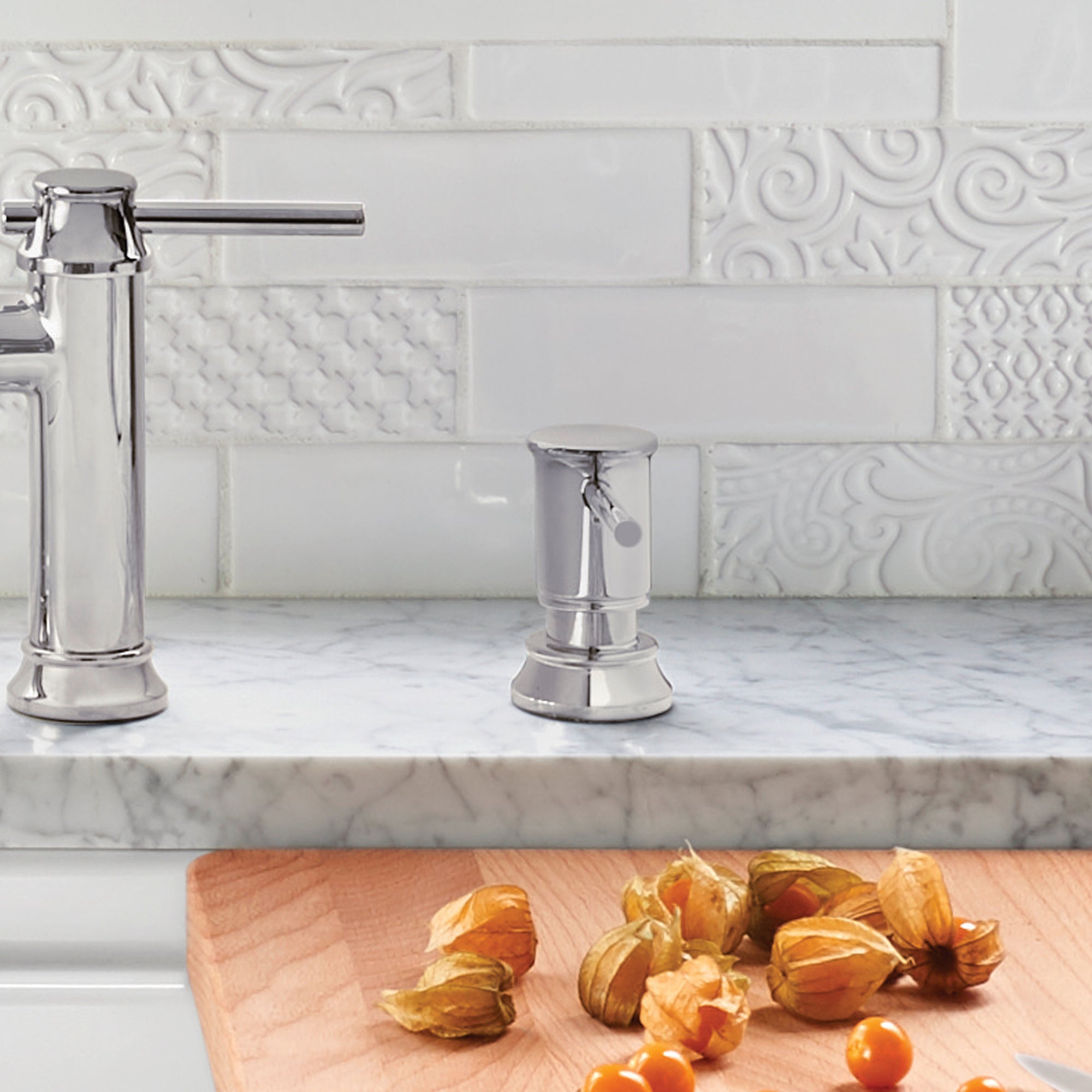 Chrome soap dispenser with cylindrical pump and round base on marble countertop next to faucet.