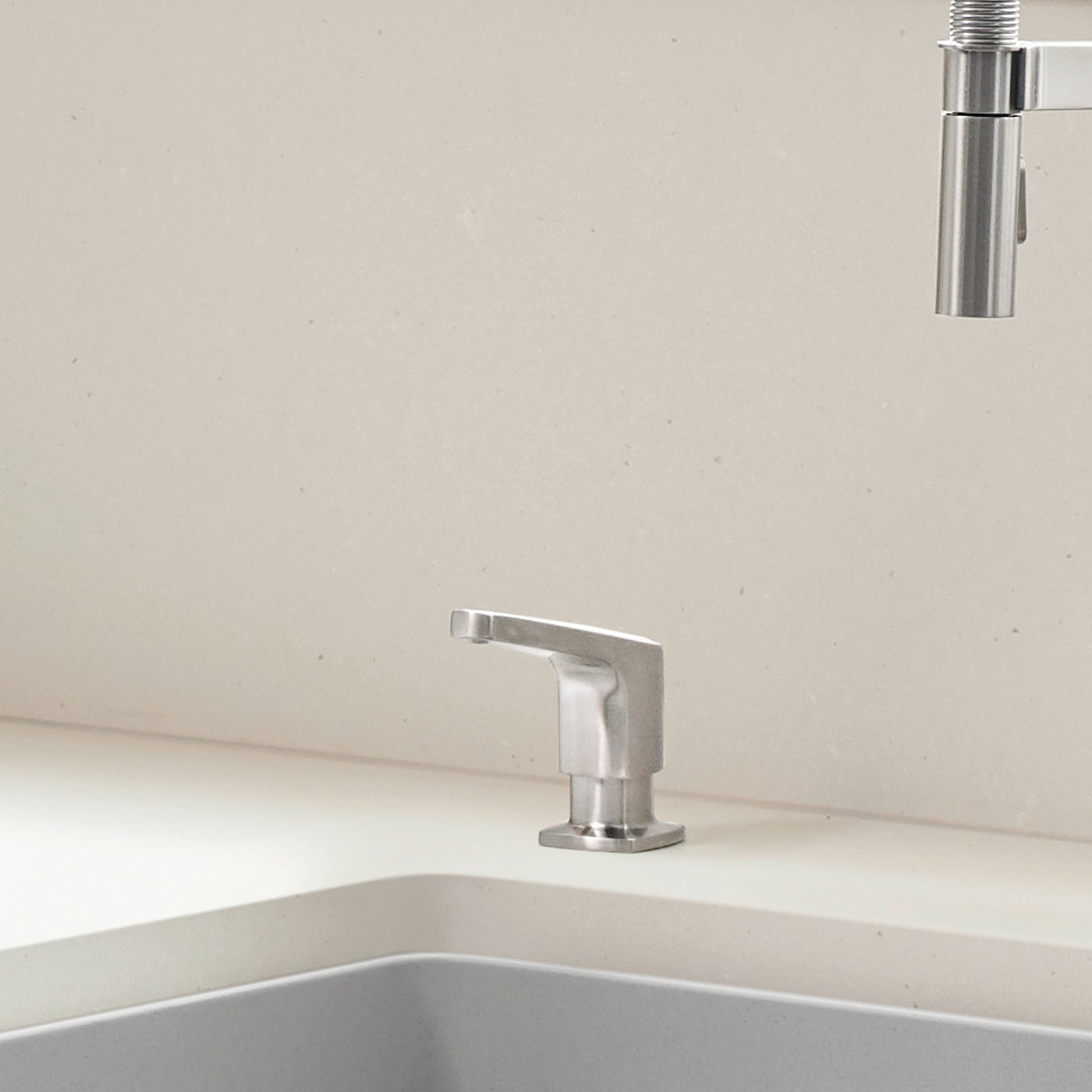 Stainless steel soap dispenser with angular spout mounted on white sink countertop.