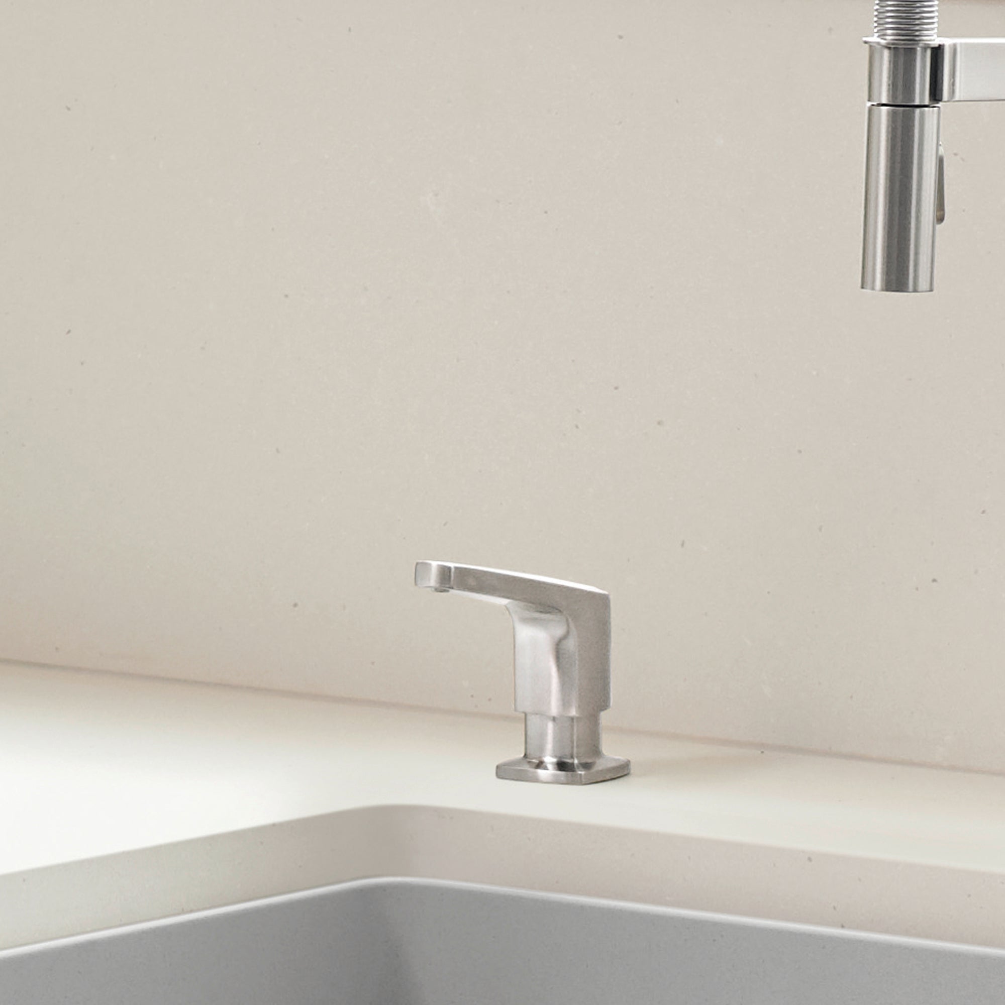 Stainless steel soap dispenser with angular spout mounted on white sink countertop.