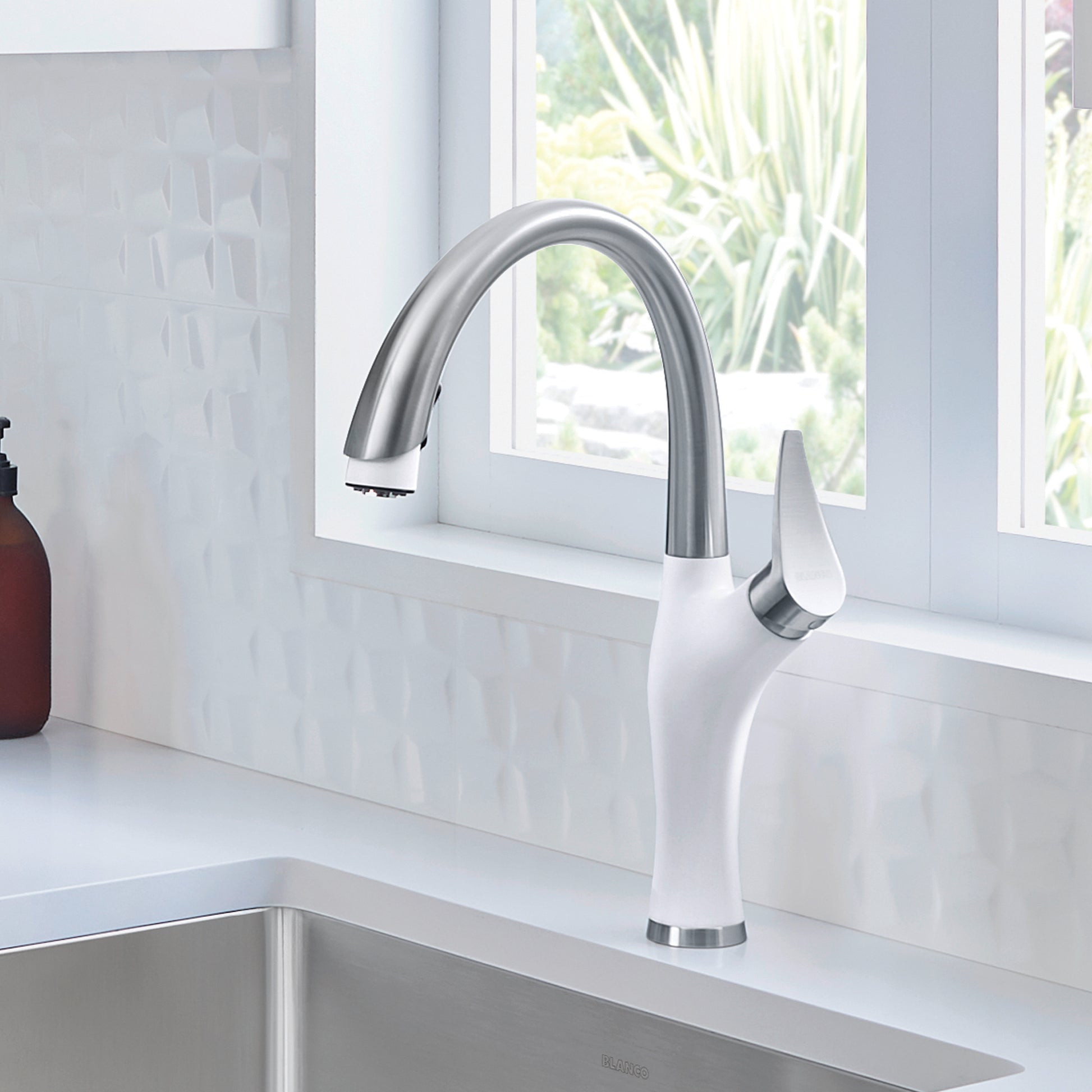 White and stainless steel kitchen faucet with curved spout and pull-down spray head mounted on countertop.