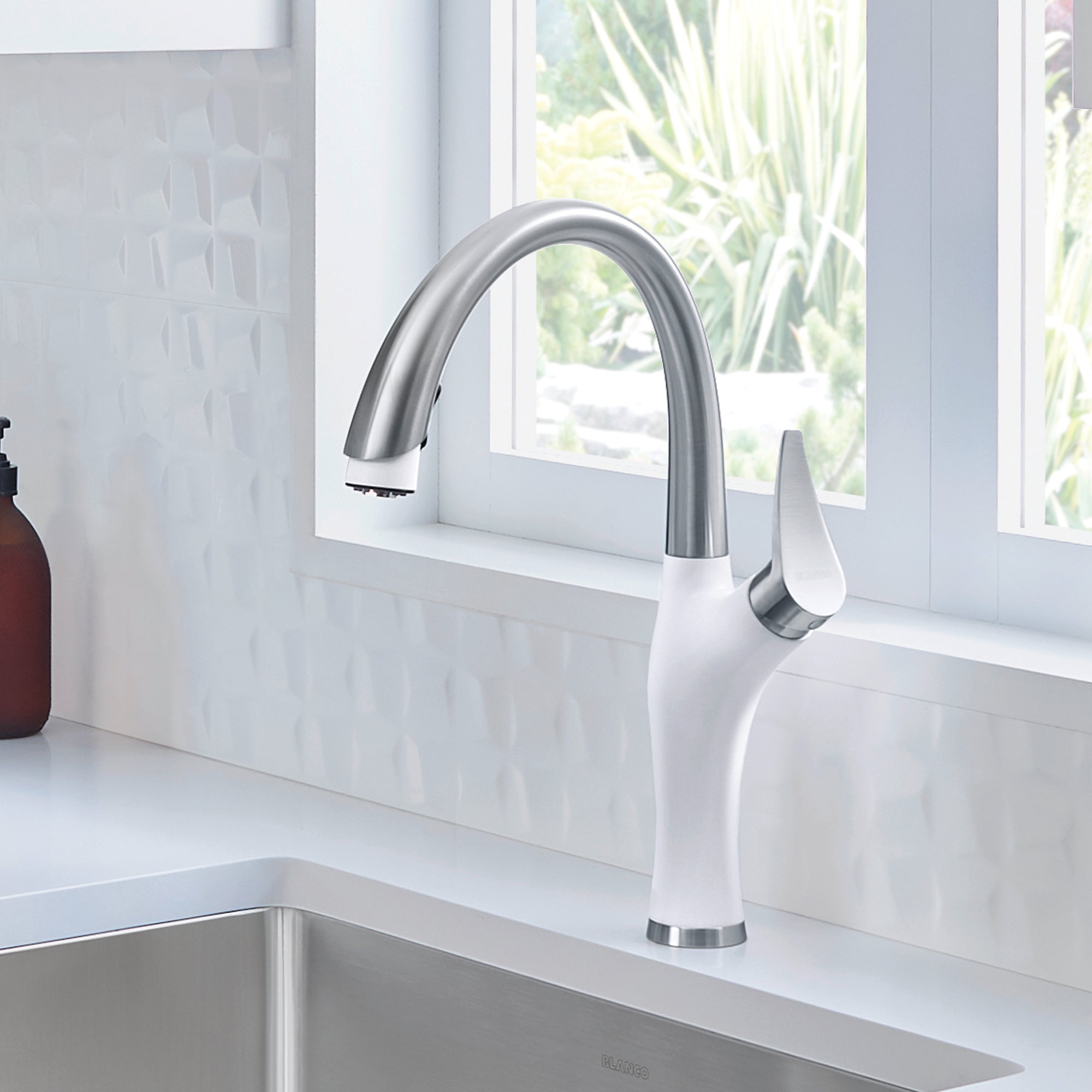 White and stainless steel kitchen faucet with curved spout and pull-down spray head mounted on countertop.