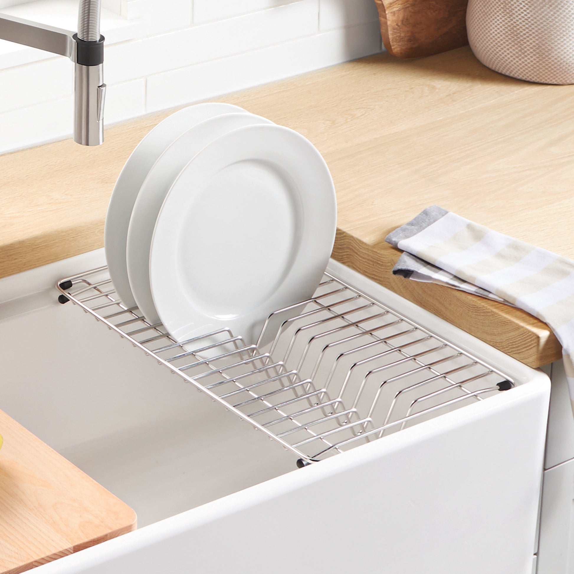 Stainless steel dish rack with plate divider positioned in white apron front sink.