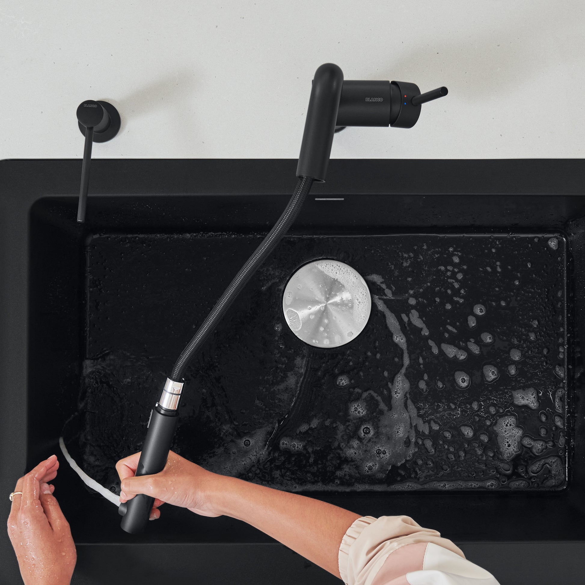 Coal black pull-out kitchen faucet with flexible hose extended over black sink basin.