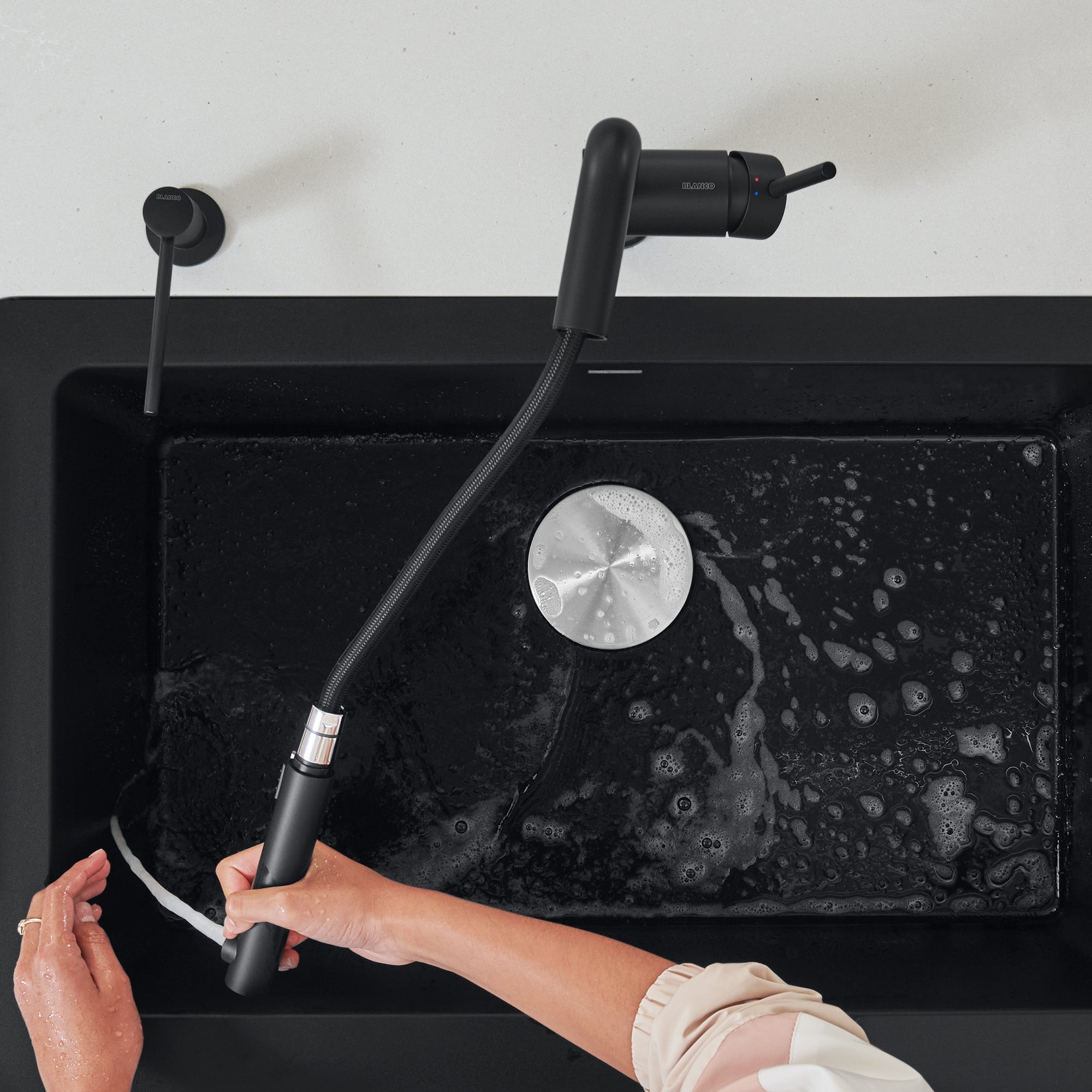 Coal black pull-out kitchen faucet with flexible hose extended over black sink basin.