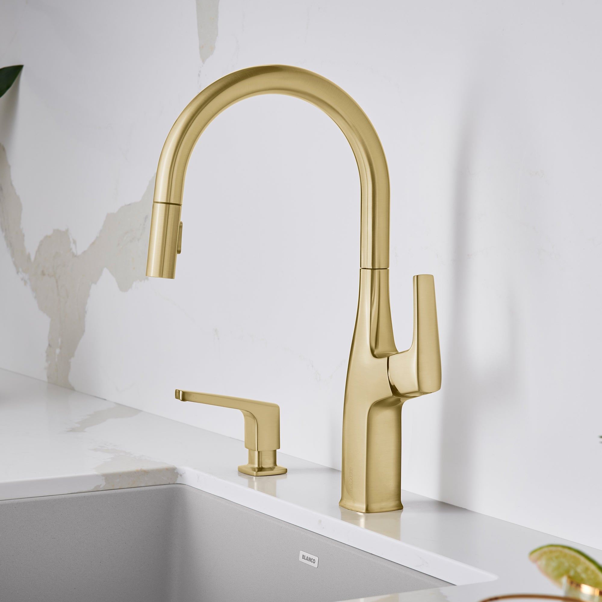 Satin gold pull-down kitchen faucet with curved spout and single lever handle, shown installed above white sink.