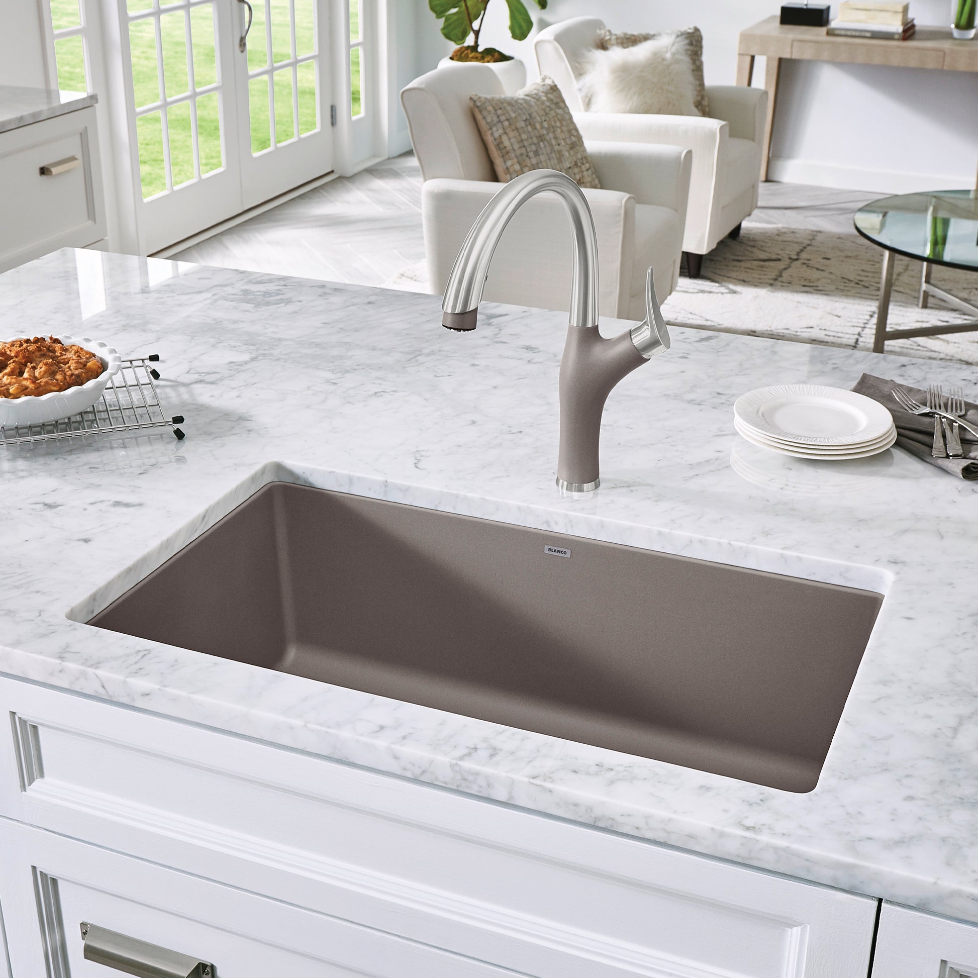 Truffle-colored single bowl undermount kitchen sink installed in white marble countertop with chrome faucet.