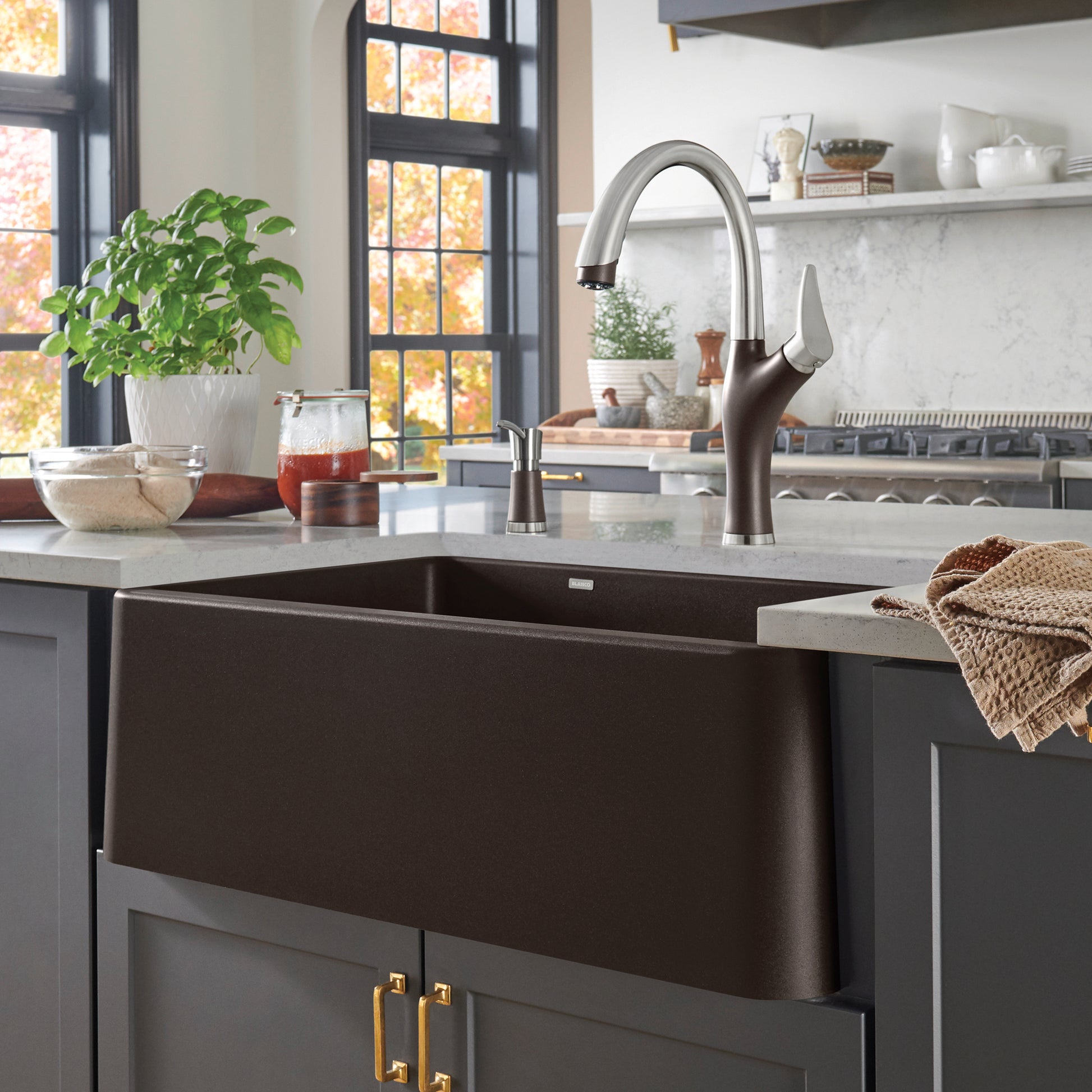 Cafe brown apron front farmhouse sink with curved stainless steel faucet installed in gray cabinetry.